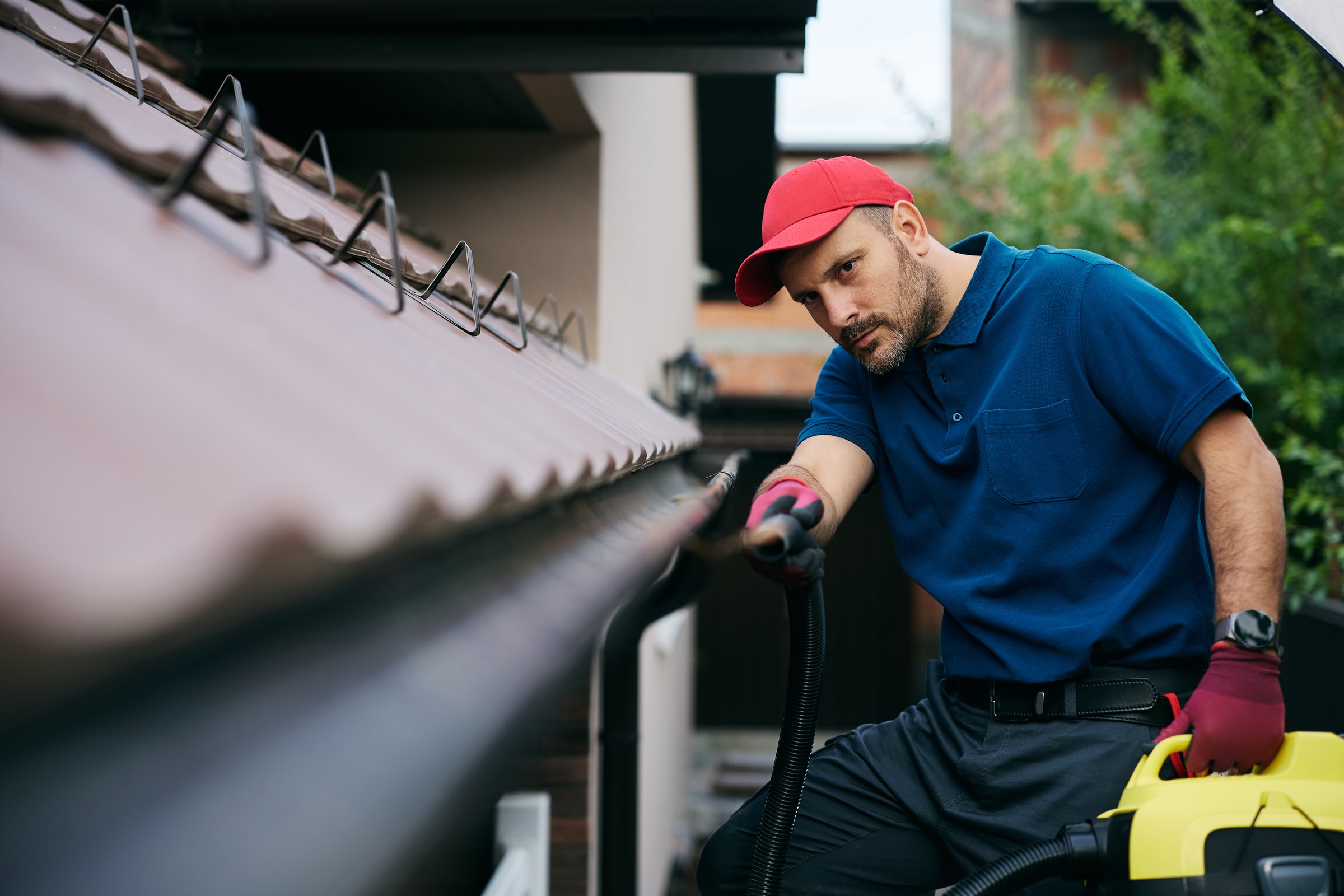 Man cleaning roof gutters to prevent clogs and water damage during autumn season. Copy space.