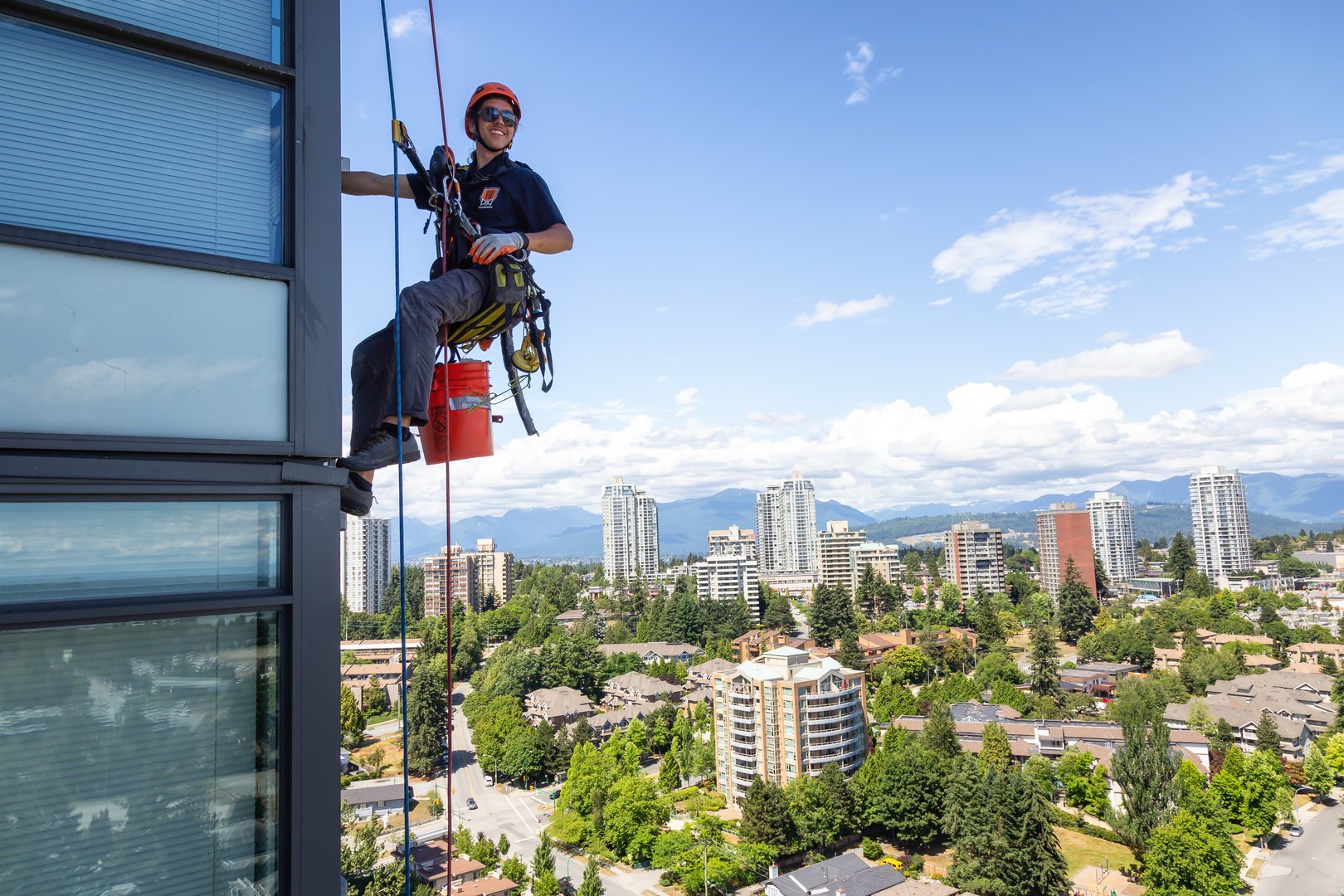 Burnaby, Vancouver, British Columbia, Canada - July 06, 2018: High rise rope access window cleaner is working during a hot sunny summer day.
