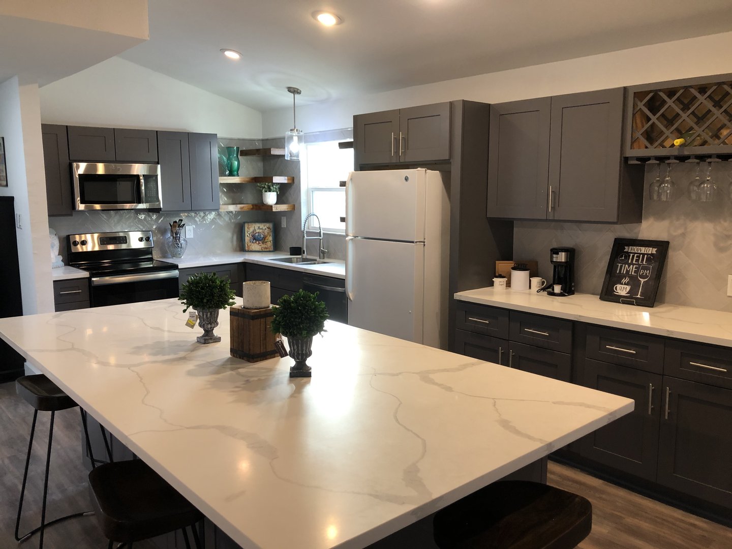Modern kitchen with gray cabinets, marble island, stainless steel appliances, and wooden bar stools.