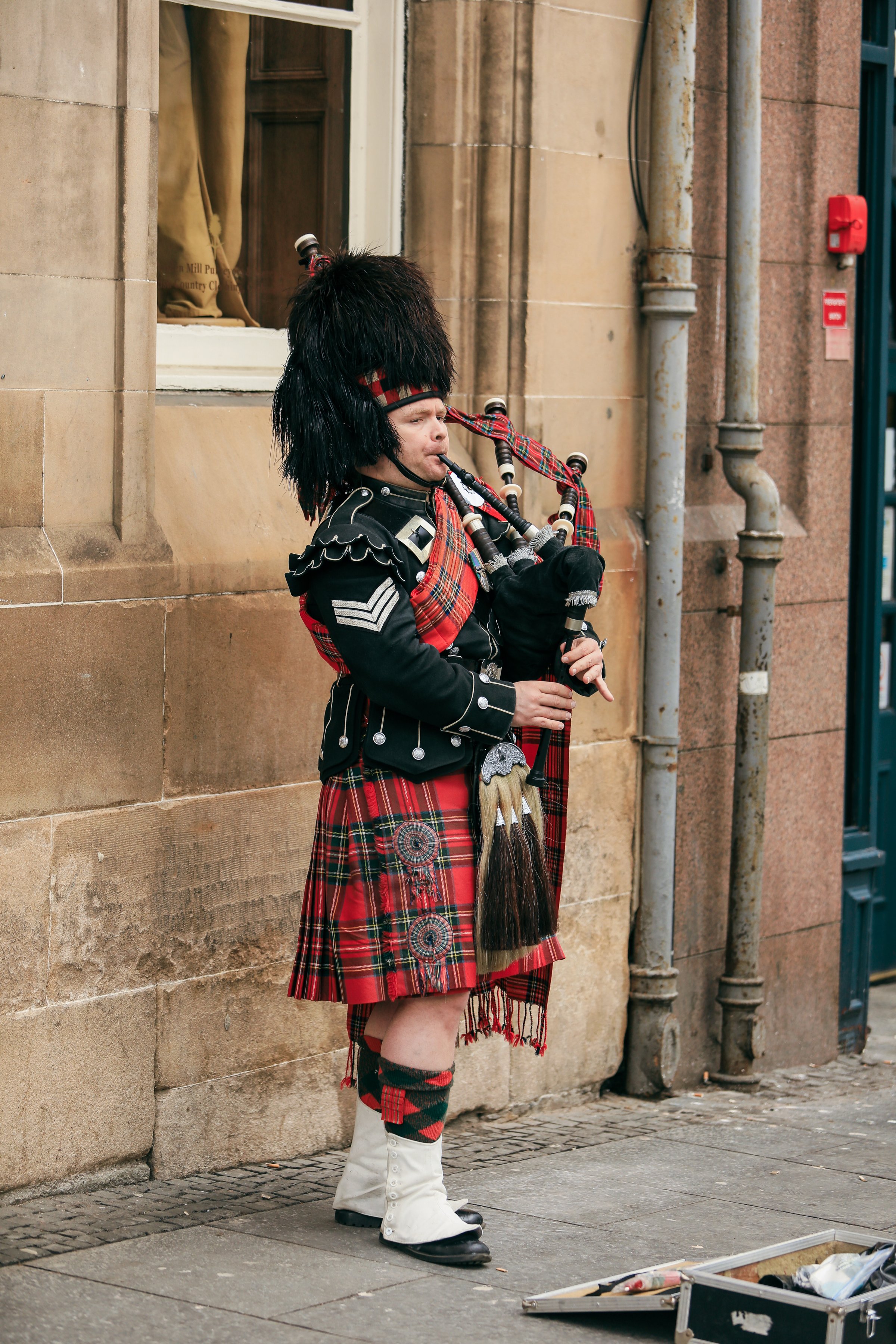 Edinburgh, United Kingdom - November 10, 2024: A talented bagpiper in full Highland dress entertains passersby on a bustling Edinburgh street amid historic architecture.