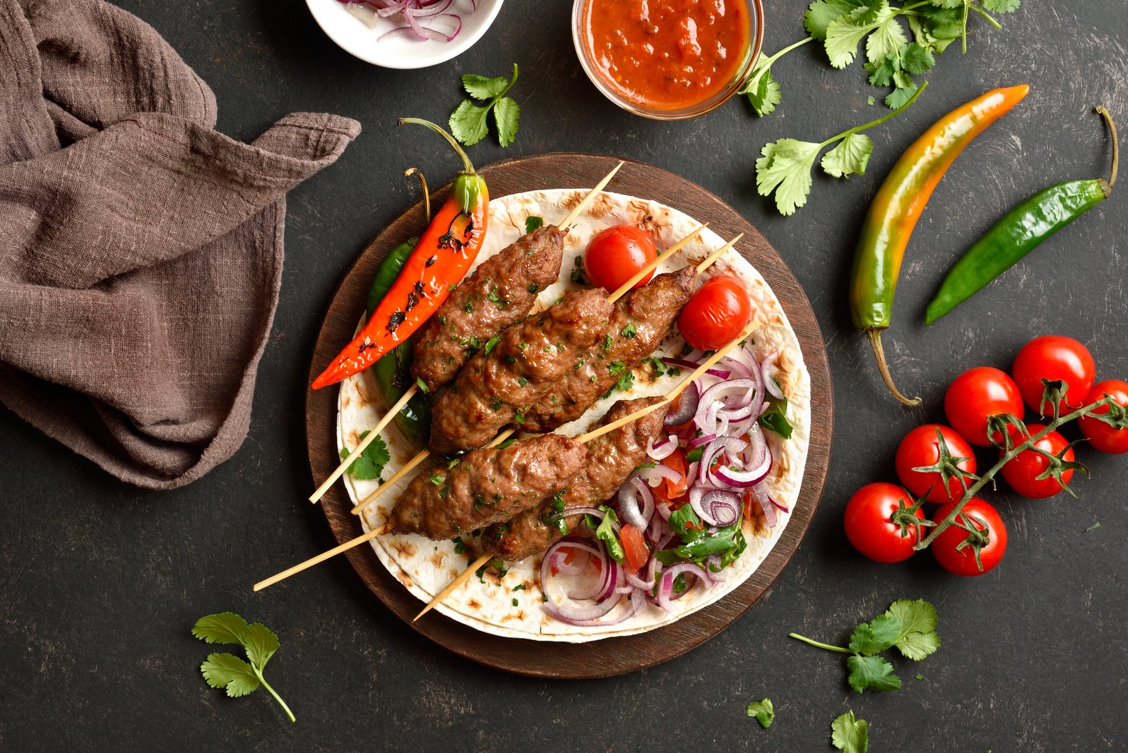 Grilled lula kebab with fresh vegetables on flat bread on wooden platter on dark background. Top view, flat lay, closeup