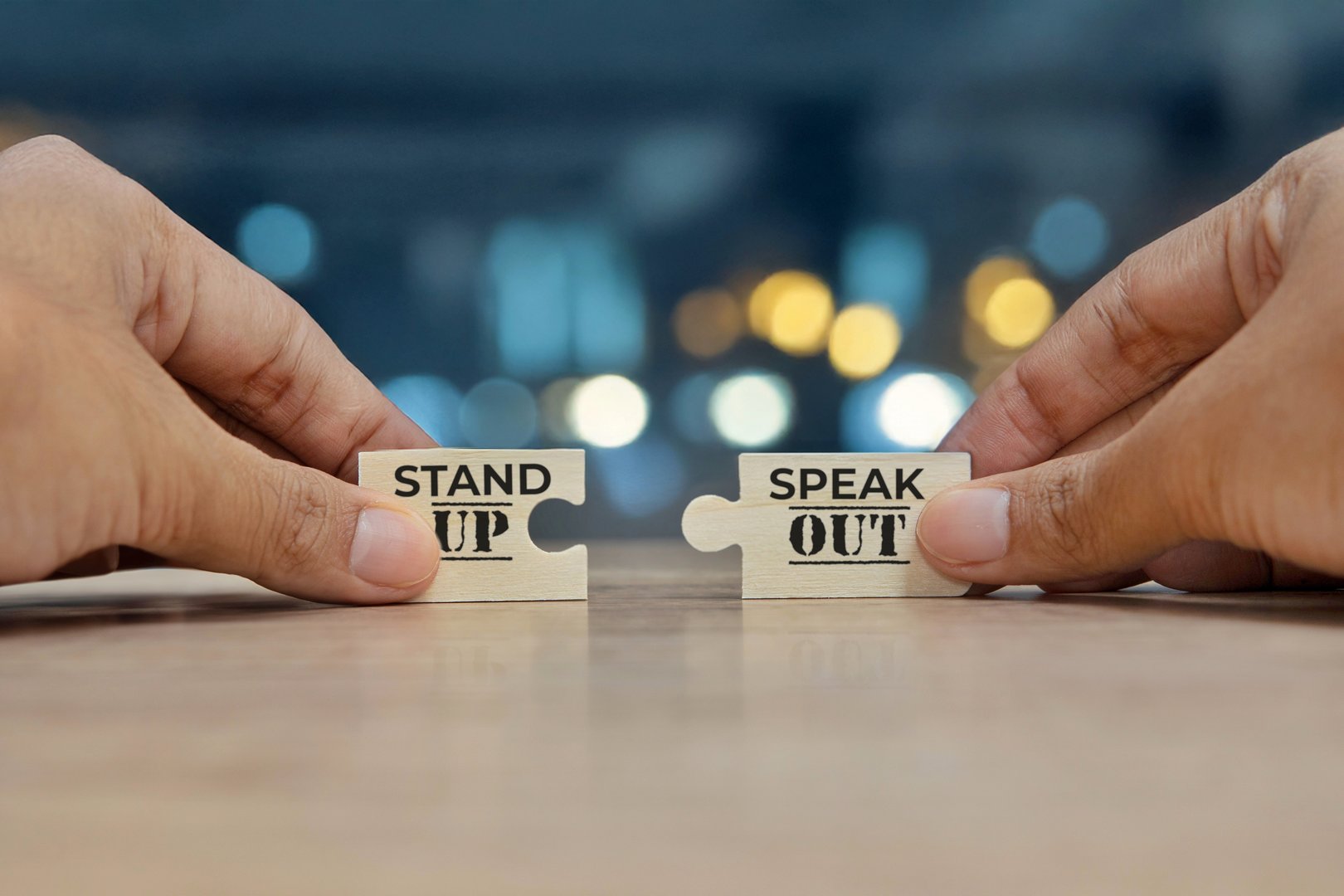 Two hands holding two puzzle pieces that fit together to form the phrase Stand Up Speak Out. The importance of taking a stand and speaking out against injustice or inequality concept.