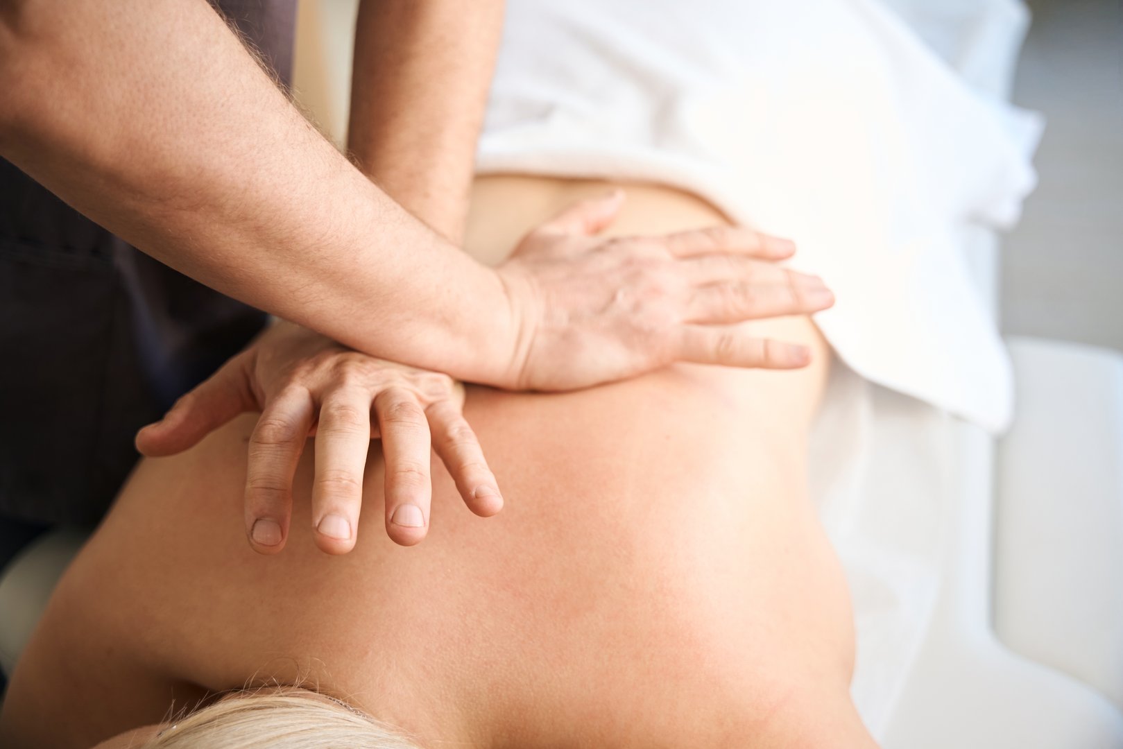 Closeup of crossed hands pressing on thoracic paraspinal muscles of client lying in prone position