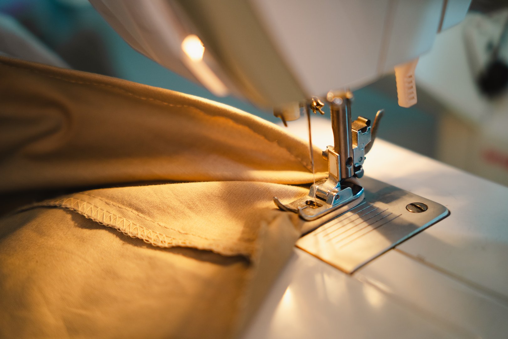 A detailed close-up shot focusing on the presser foot of a sewing machine as it stitches beige fabric