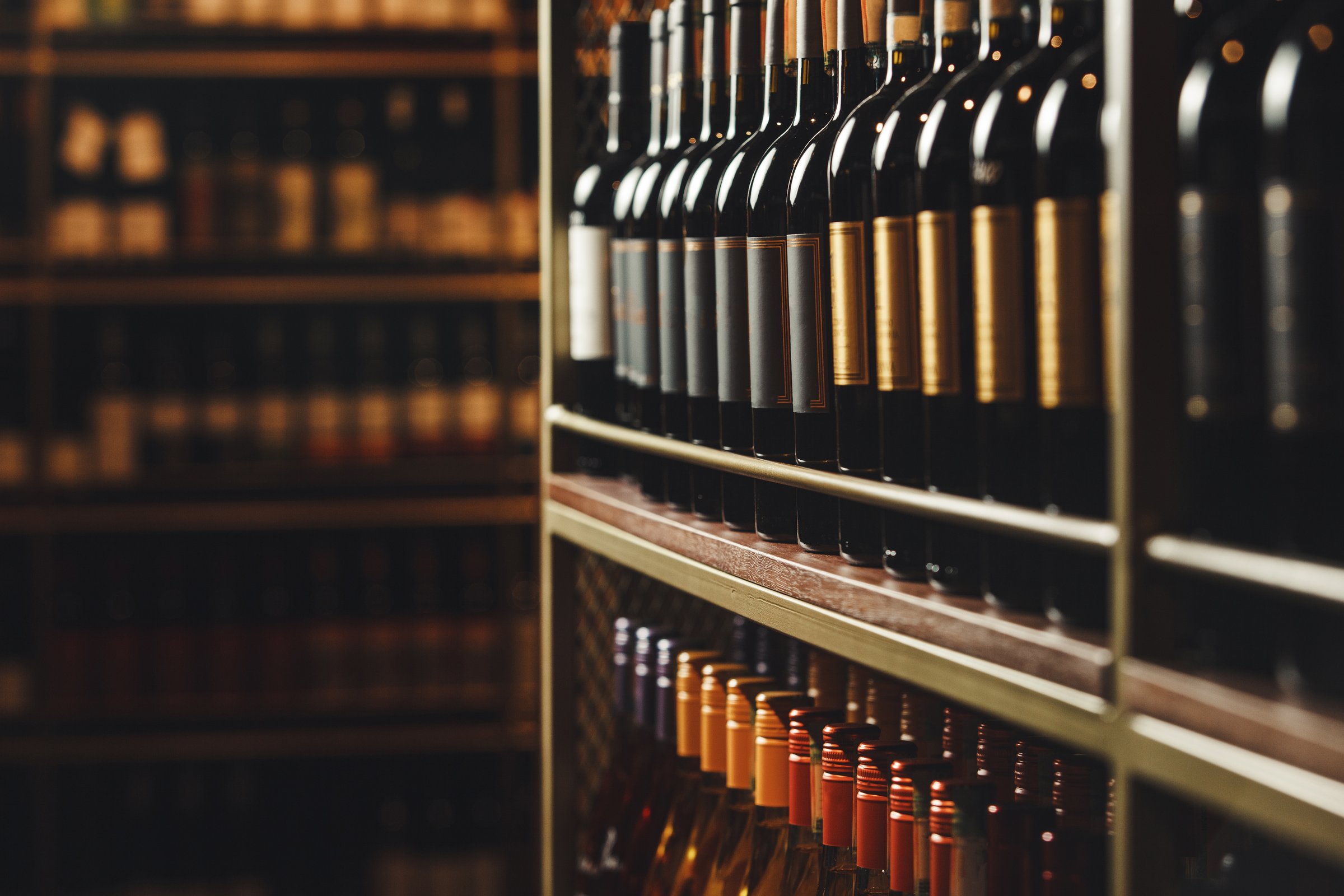 Rows of filled elite wine bottles are showcased on wooden shelves, indicating private and well-curated collection. The subtle lighting accentuates bottles sophisticated labels and the rich colors of glass, conveying an ambiance of exclusivity and luxury in serene cellar environment.