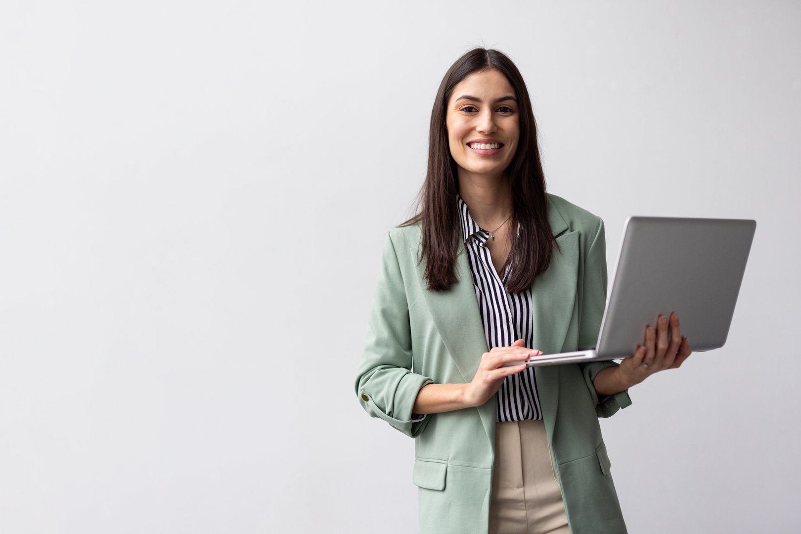 Portrait of a young businesswoman holding a laptop and smiling at the camera on a white background