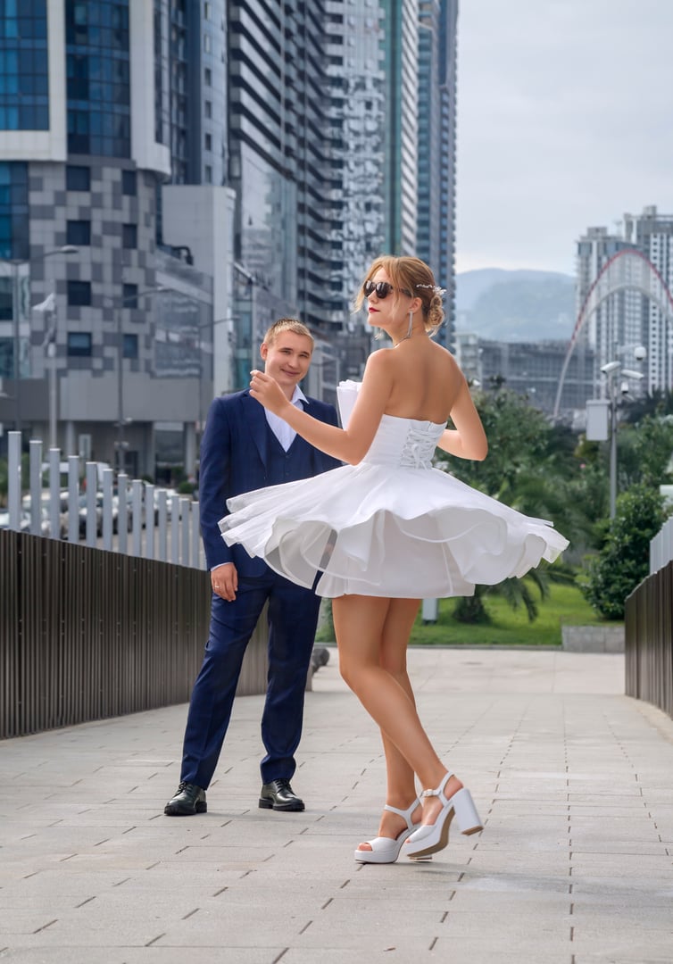 The groom looks at the bride, who is spinning on the bridge in her white dress. Full height