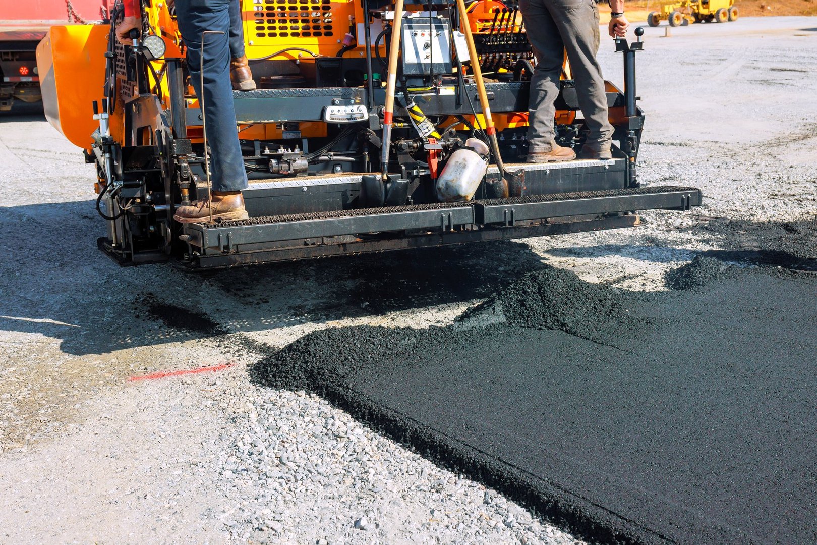 Workers operate paving machine to lay new asphalt on construction road site