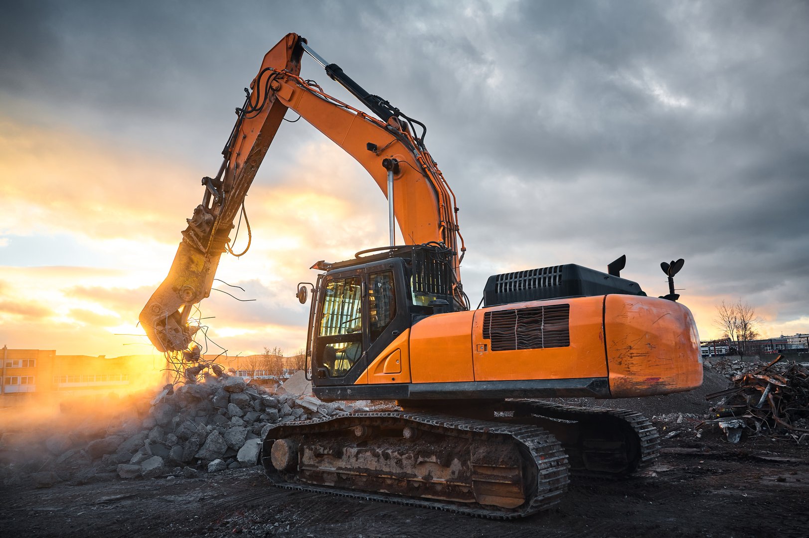 Powerful crusher on excavator rigging destroys armored cement leftovers for recycling at demolition site at sunset light closeup