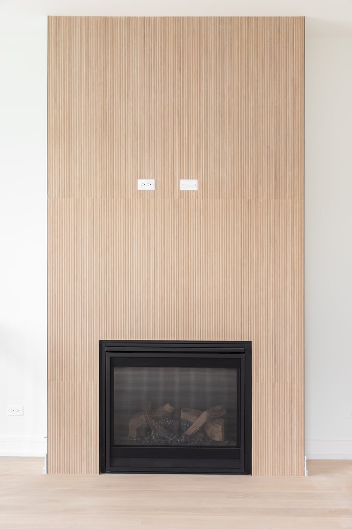 A modern fireplace with with floor to ceiling white oak wood slats, white oak flooring, and a black electric fireplace.