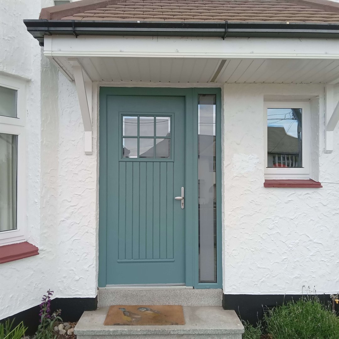 Blue front door with glass panel and window on white stucco house, with a small overhang and doormat.
