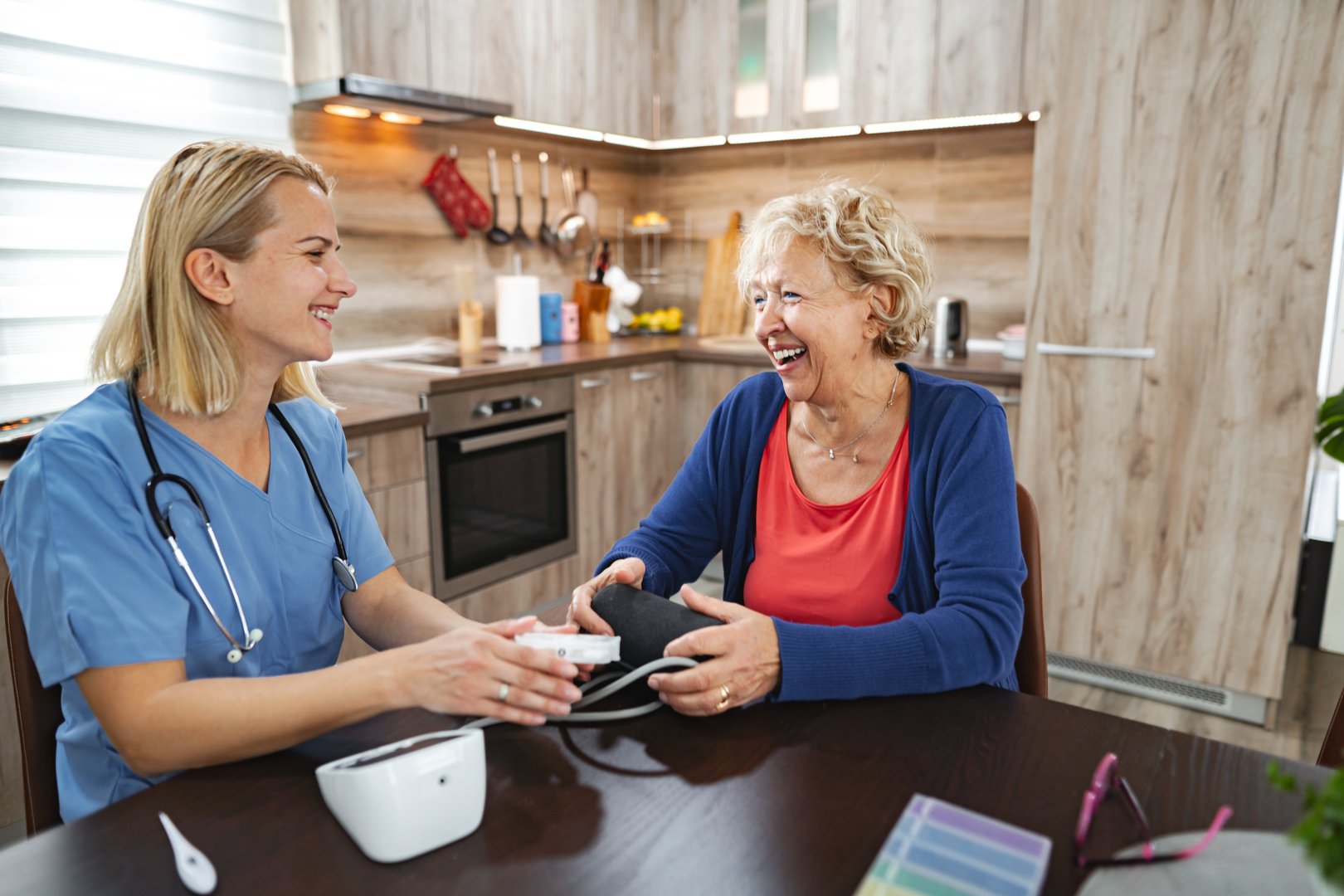 A nurse checks the blood pressure of an elderly woman in a warm kitchen.