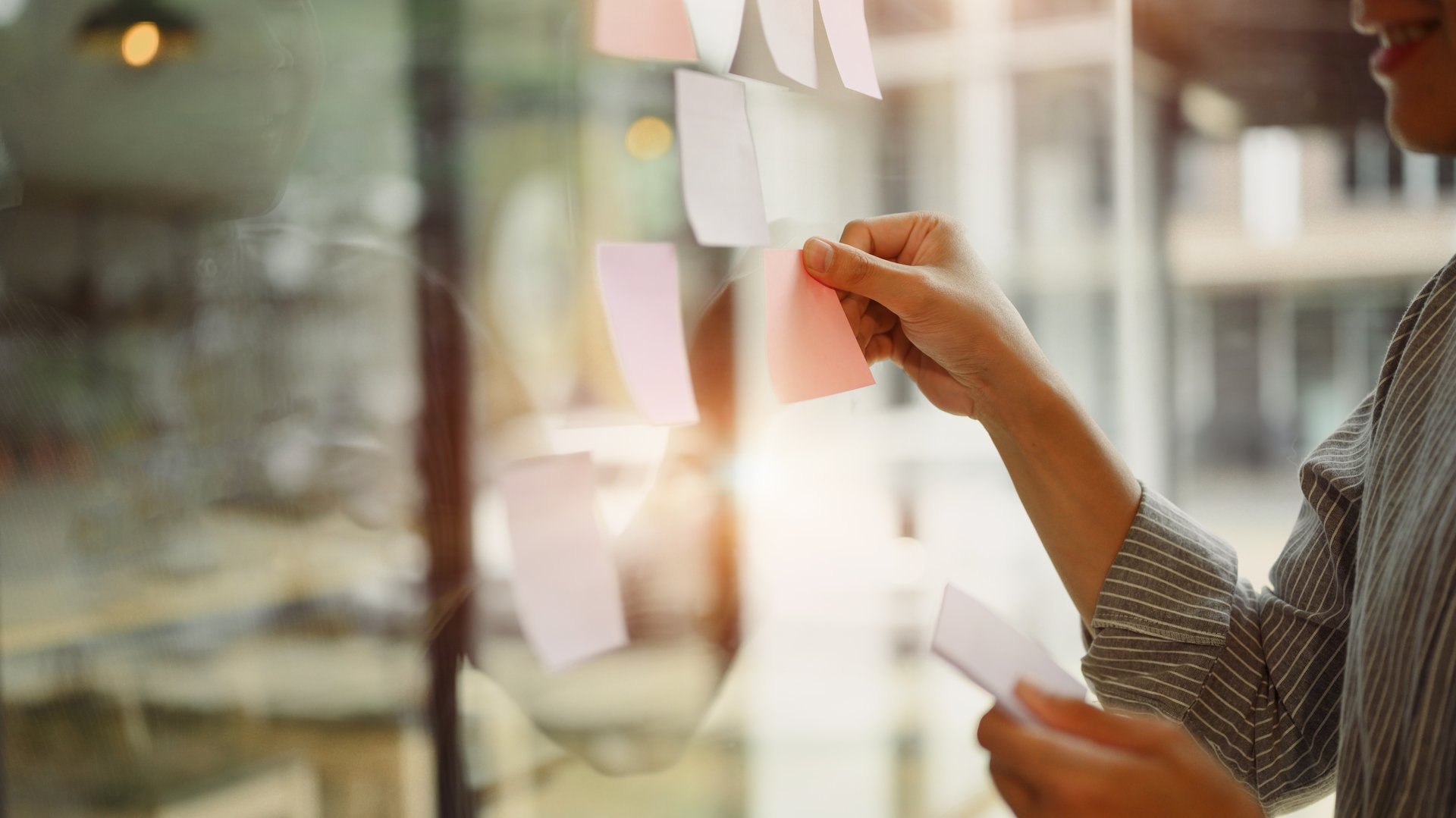 Businessman placing colorful paper notes on transparent board during team strategy session.