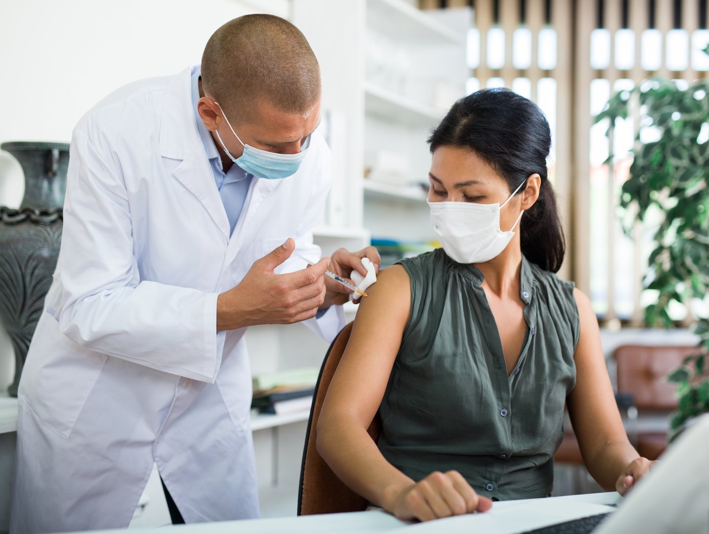 Focused professional doctor vaccinating asian businesswoman at work desk in office. Concept of protecting against viruses and preventing spread of Covid-19