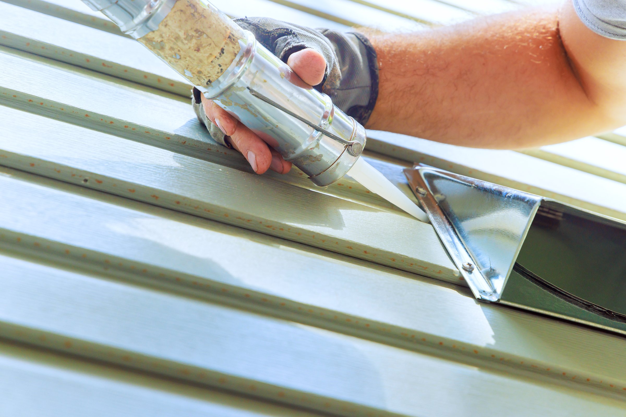 Contractor is sealing metal siding with caulk gun in home renovation project under construction