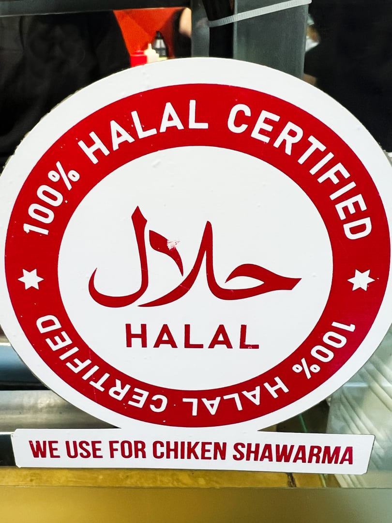 Sign indicating 100% halal certification is shown at a shawarma counter. Use of chicken in the preparation, catering to halal conscious consumers and promoting halal food practices.