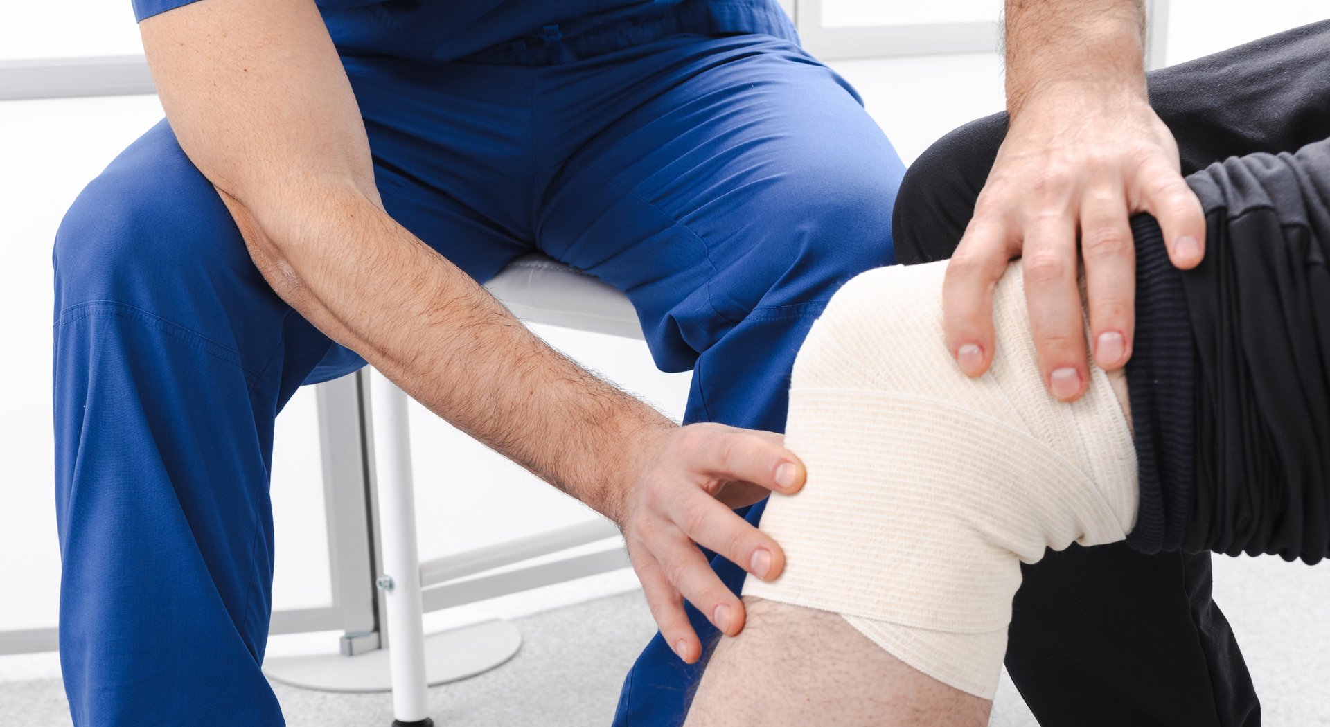 Osteopath examines man's knee with elastic bandage in rehab medical center. Joint, knee, and leg pain treatment