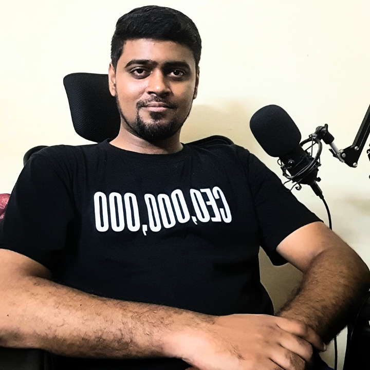 A man sitting in a chair with a microphone, wearing a black T-shirt that says 'CEO, 000,000'.