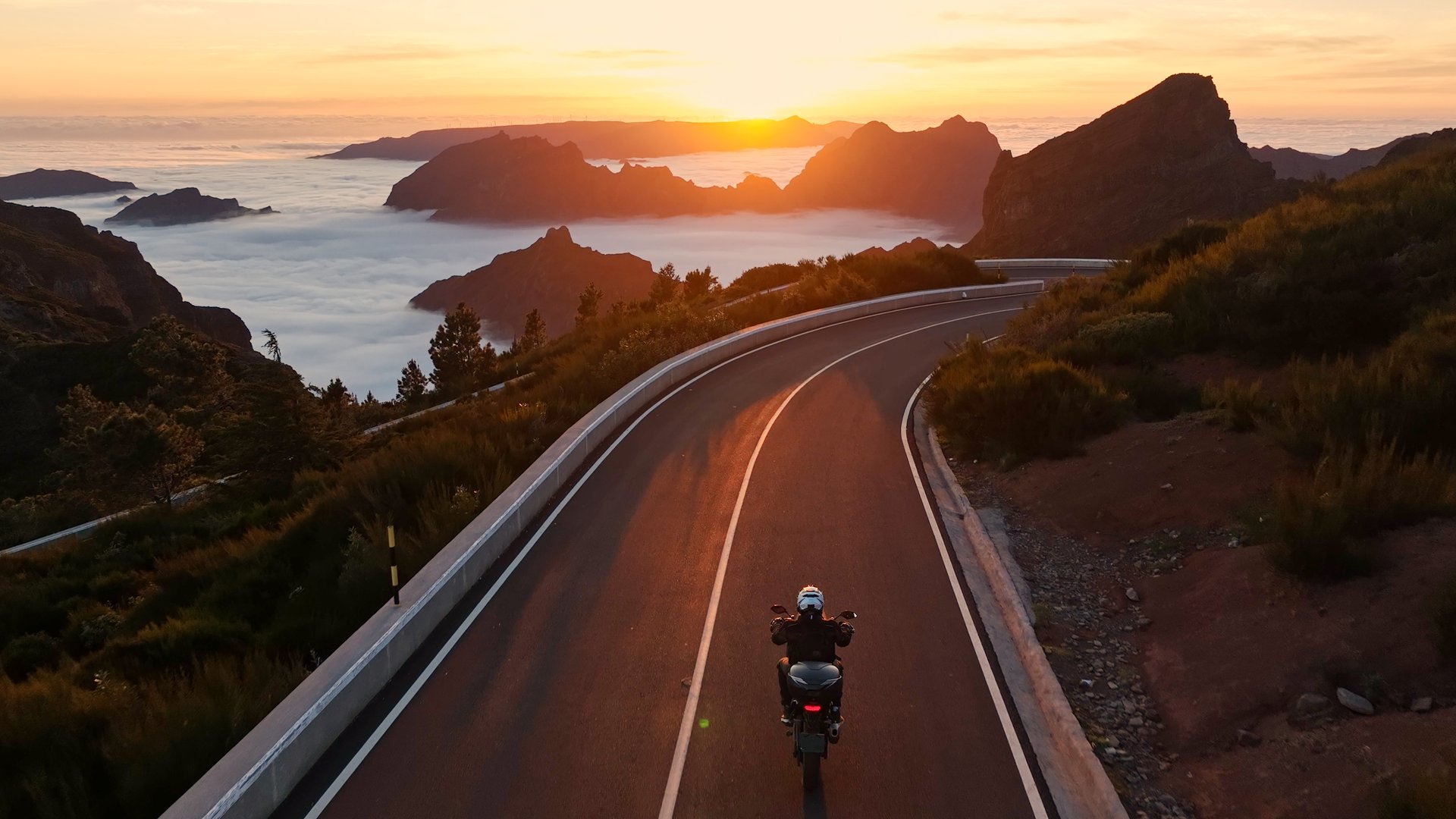 Epic Sunset View in High Mountain Landscape with Motorcycle Driver Riding on Asphalt Road . Pico do Arieiro , Madeira Island . Clouds in the Valley .