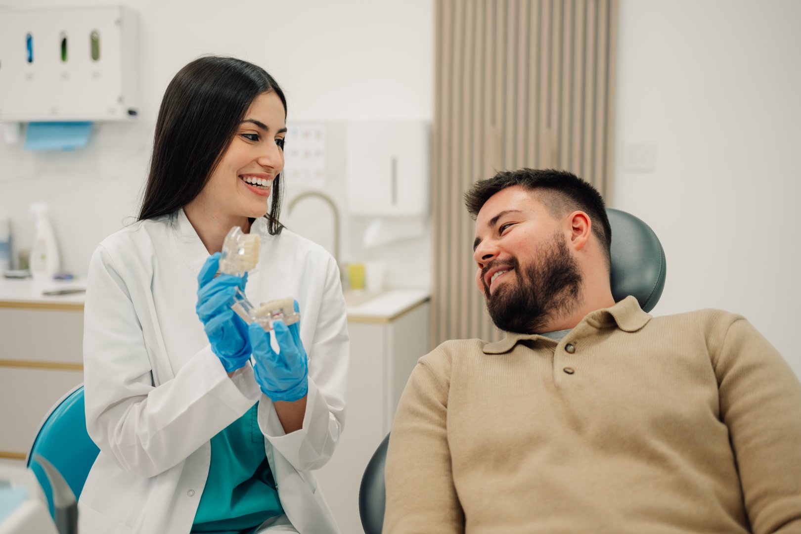 Female dentist explaining to male patient the treatment using a teeth model in a dental clinic