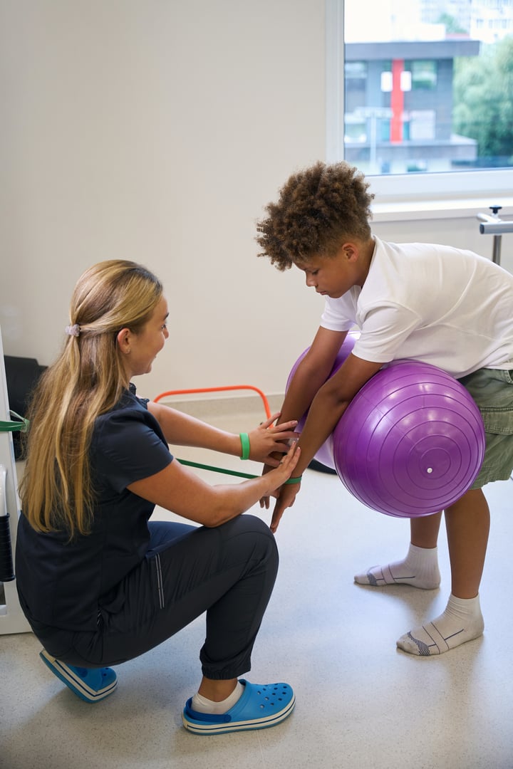 Professional physiotherapist supervises a young patient using exercise ball for a strength and coordination exercise, focusing on maintaining proper form.