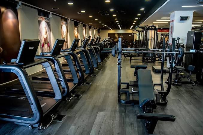 Modern gym interior with rows of treadmills, weightlifting benches, and exercise equipment under ambient lighting.