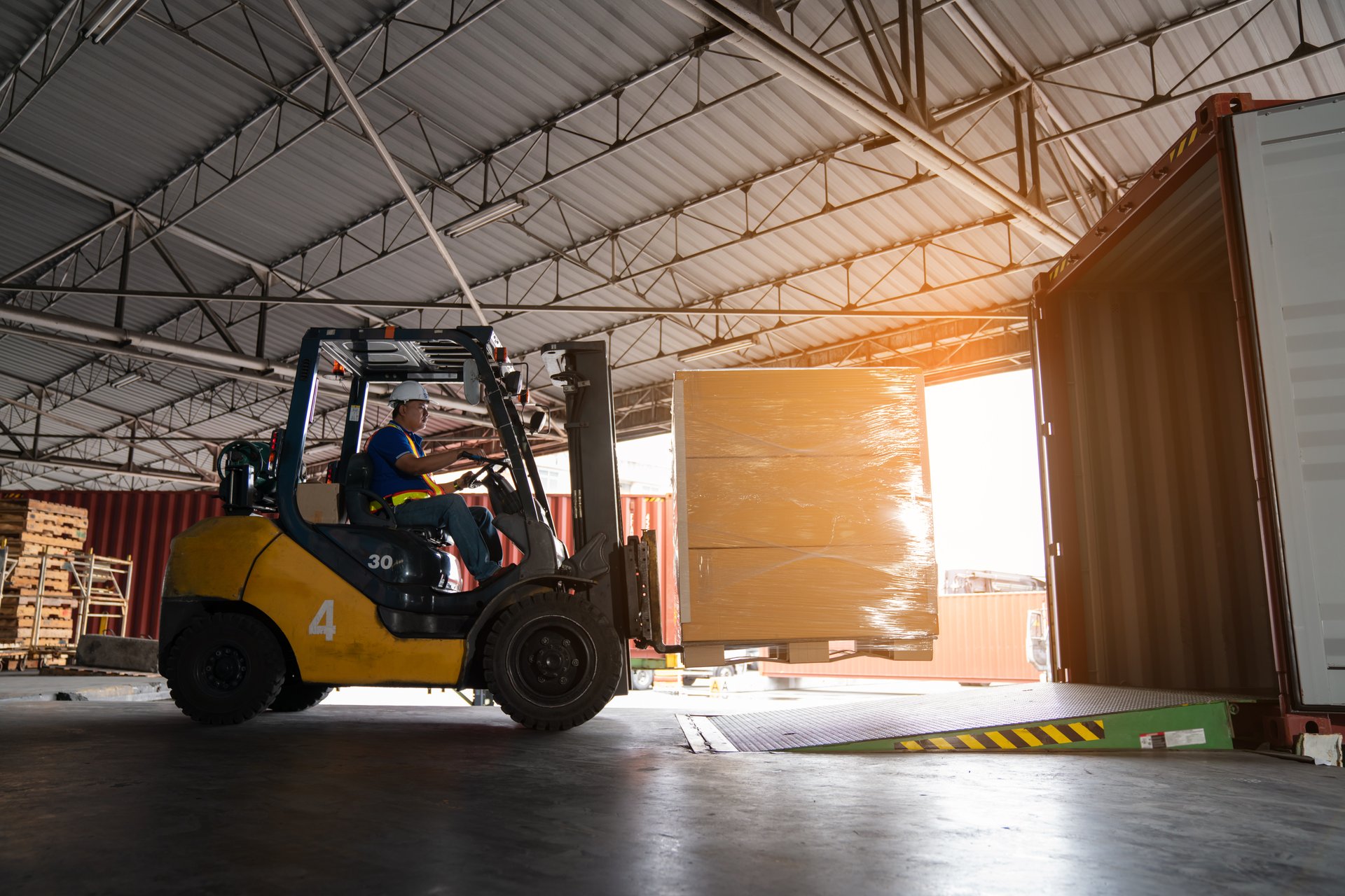 Warehouse worker driver in uniform delivery and loading pallet product by forklift.