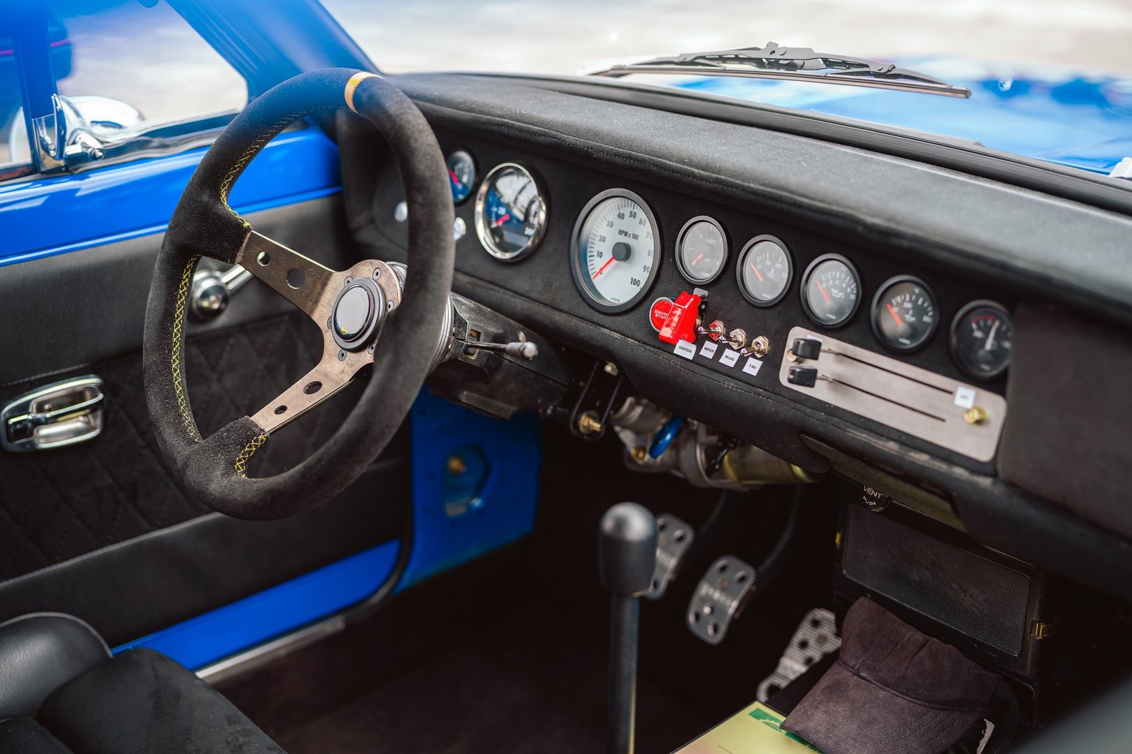 Close-up view of the interior of a vintage racing car focusing on the steering wheel and dashboard. The image shows detailed gauges, sporty design elements, and presents a retro automotive theme.