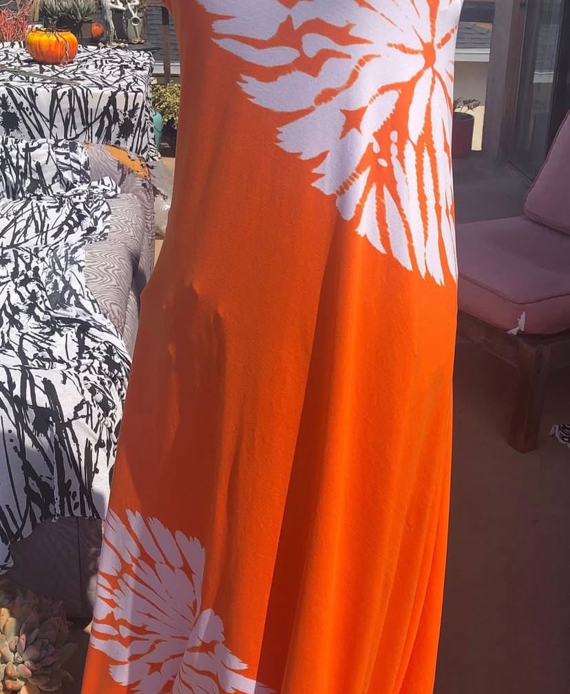 Orange tie-dye dress with white flower patterns draped over a chair, outdoor setting.