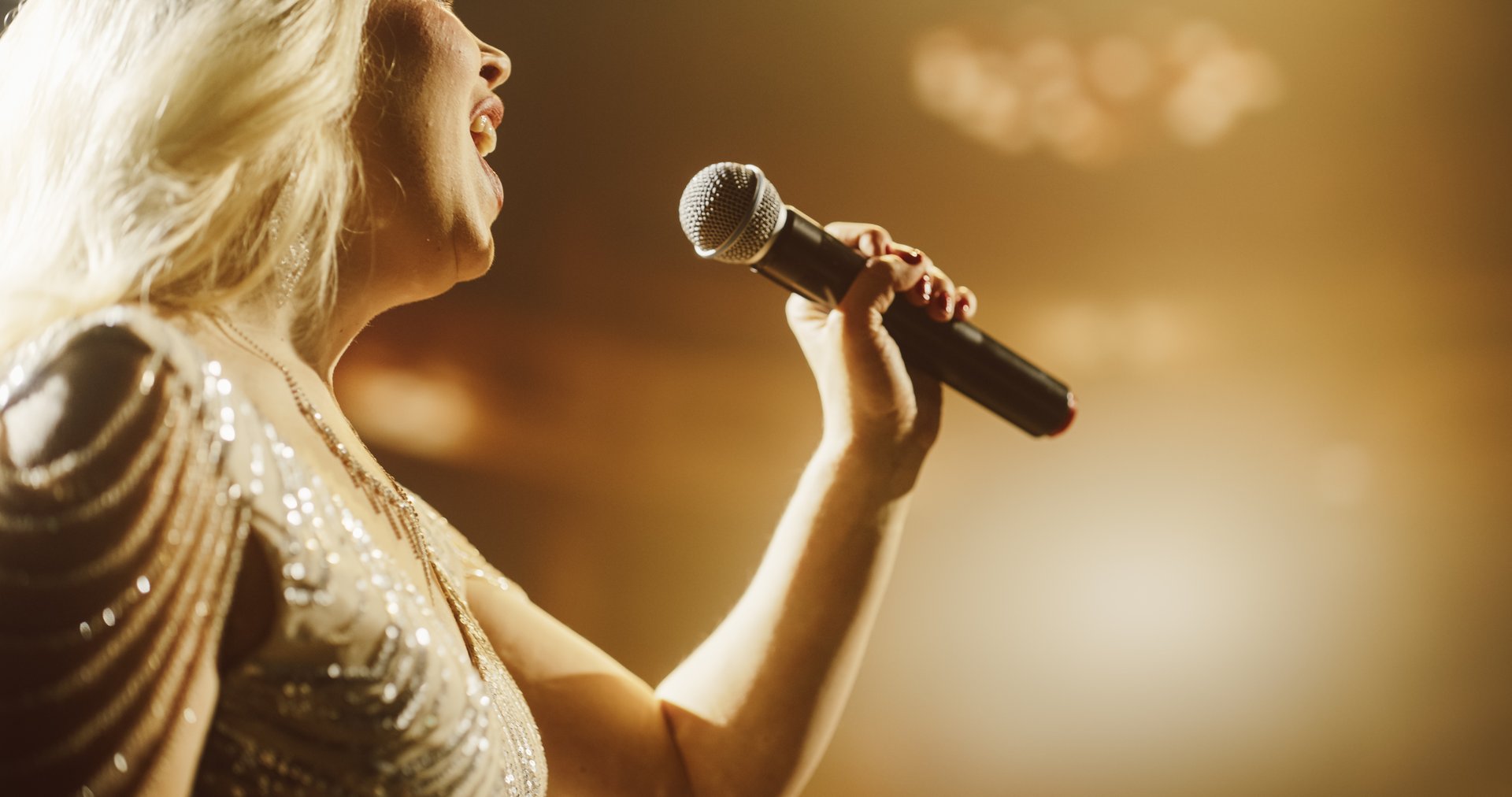 Close Up Portrait of a Blonde Musician Using a Microphone to Sing a Powerful Pop Song in a Beautiful Warm Lit Venue. Female Music Performer Putting On a Show at a Concert Stage