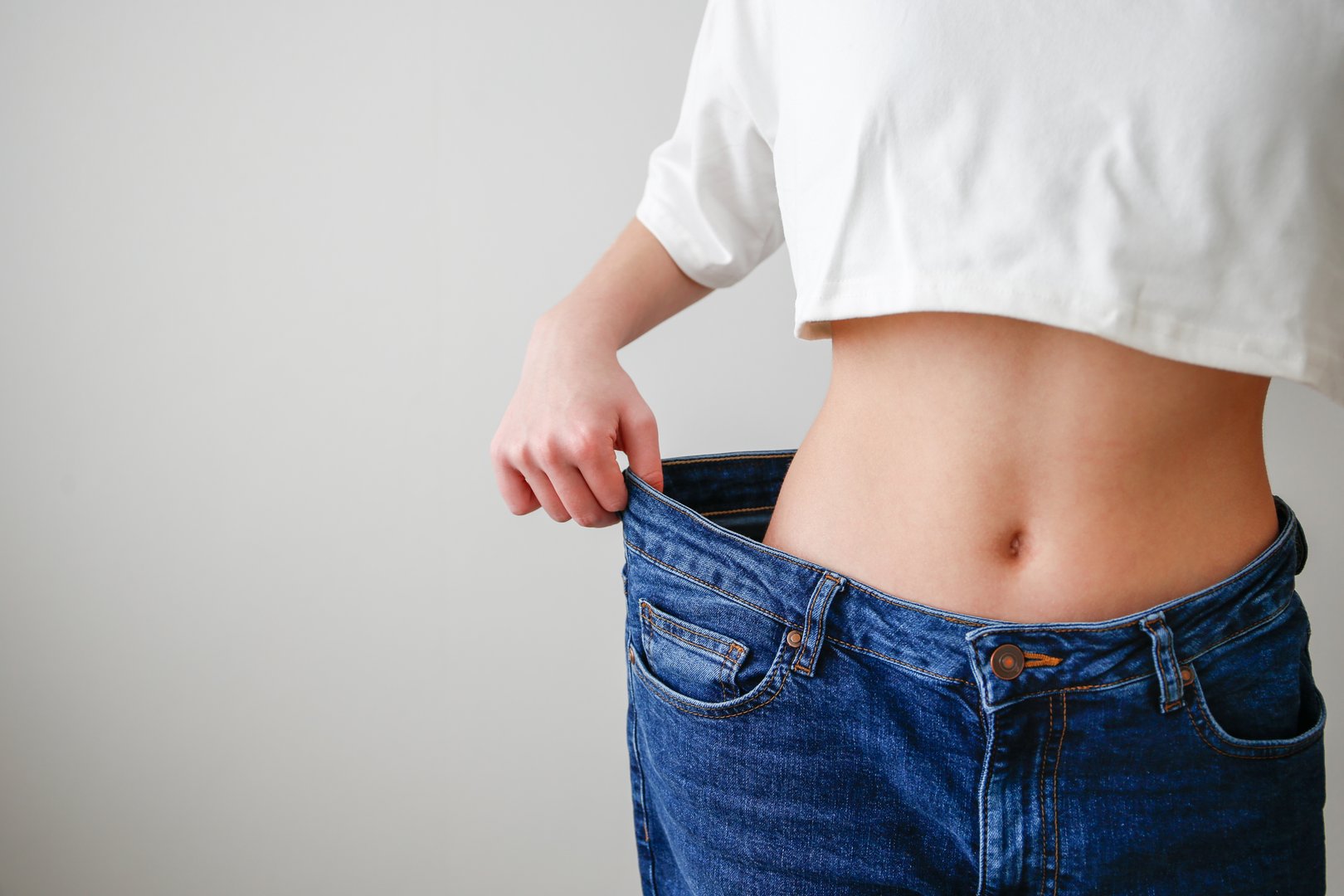 A teenage girl in huge jeans on a gray background. Weight loss. Diet in adolescence.