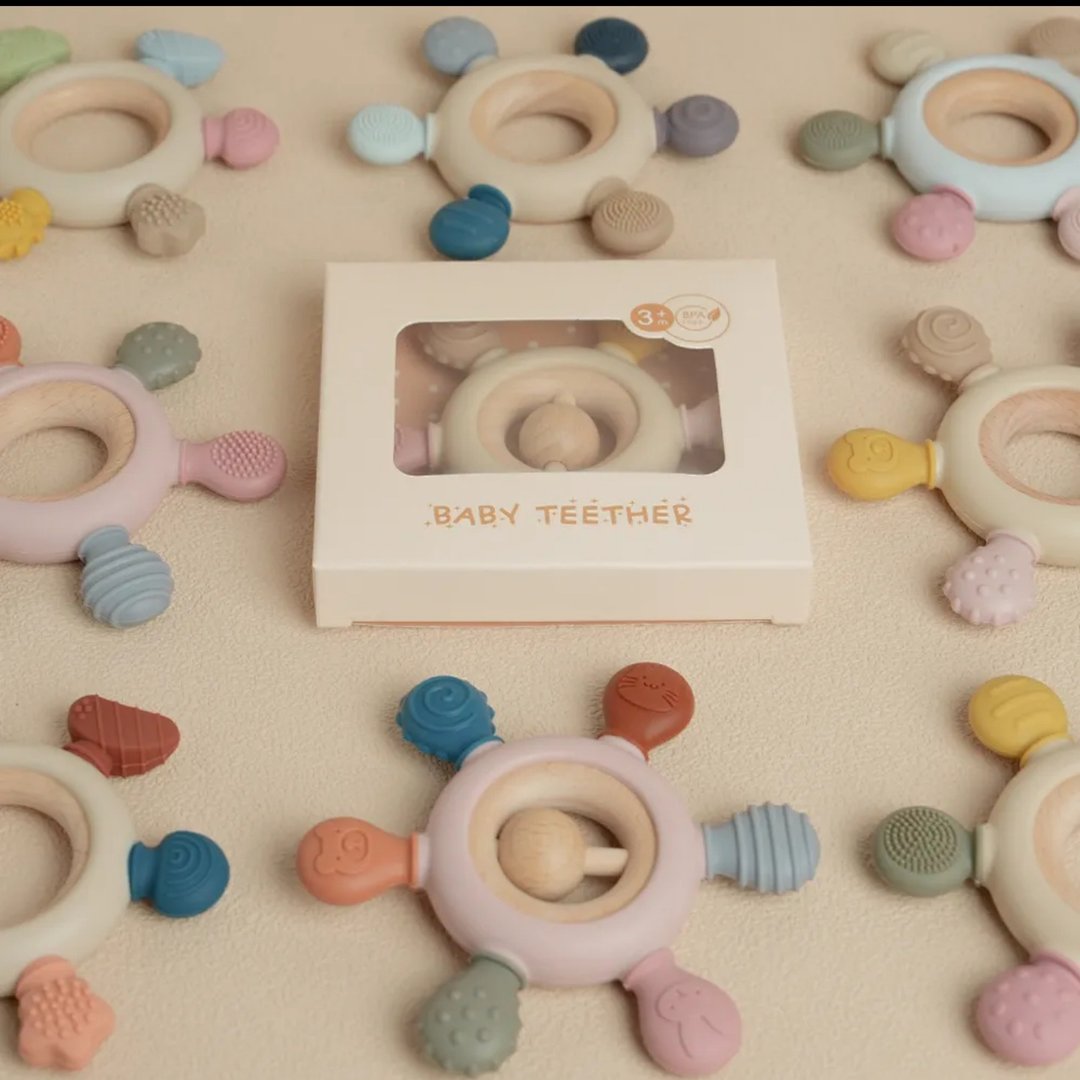 Colorful circular baby teethers with varied textures and colors arranged around a boxed teether on a beige surface.