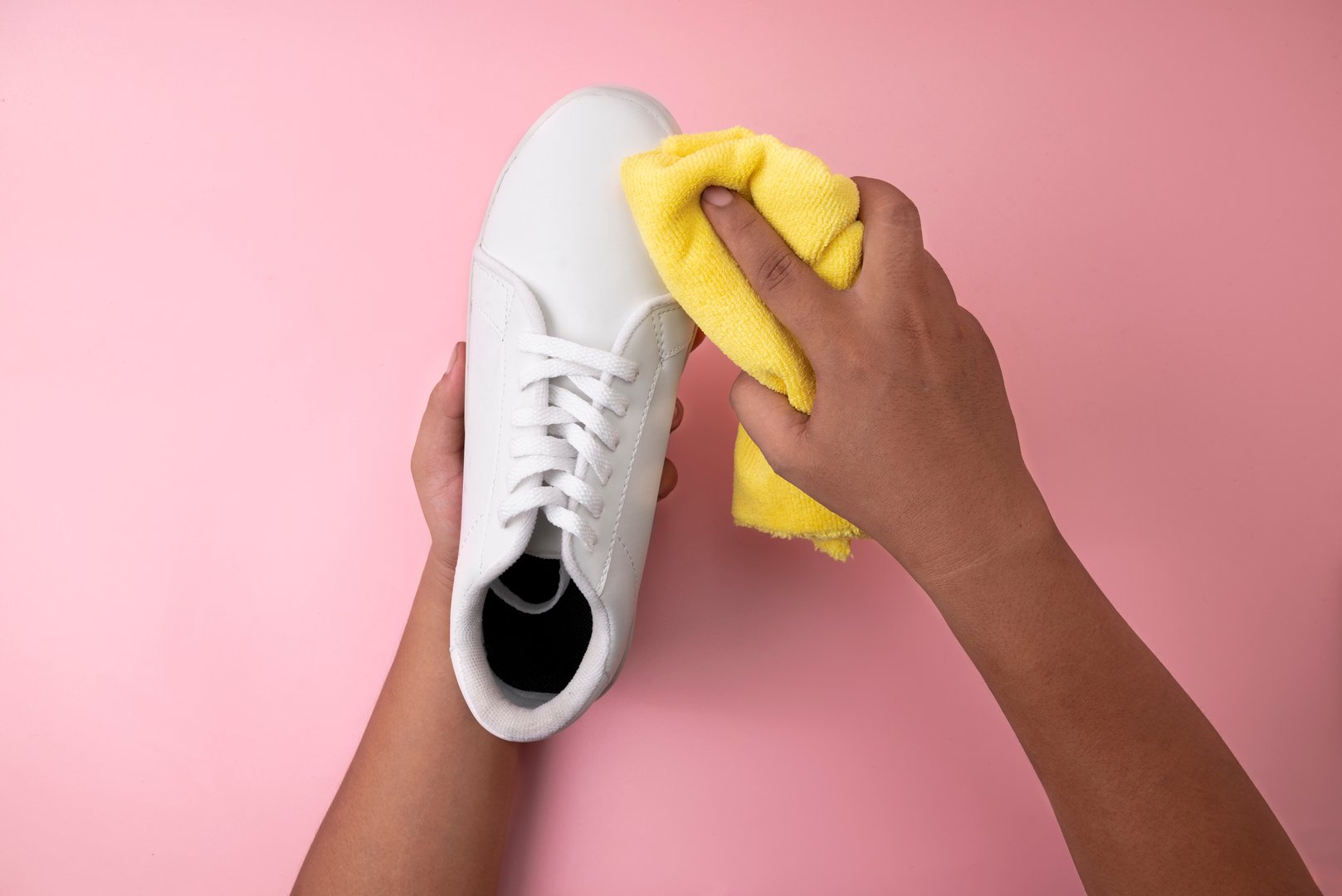 Human hand cleaning white sneakers with a microfiber cloth. Shoe care concept