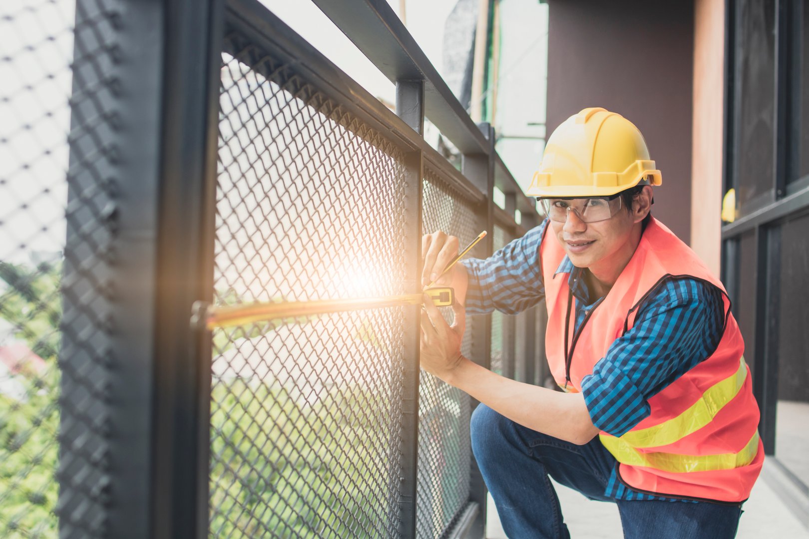 Portrait Of Smiling Engineer Measuring Railing On Balcony At Construction Site