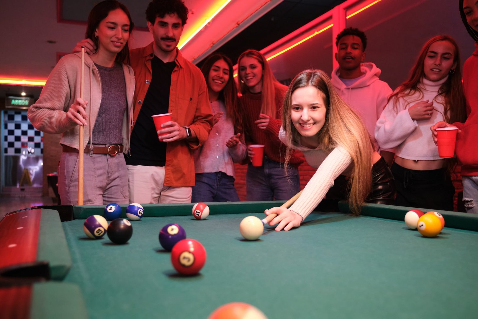 Young woman playing pool with friends cheering her on in a pub, they are having fun