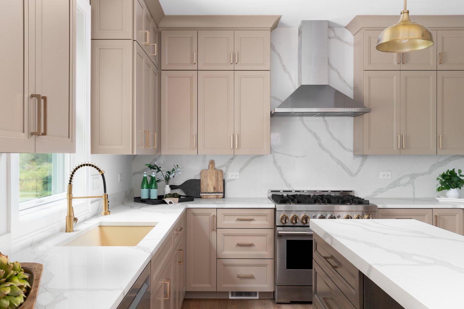 A kitchen detail with brown cabinets, marble countertop and backsplash, wood island, and gold faucet, sink, and light fixtures.