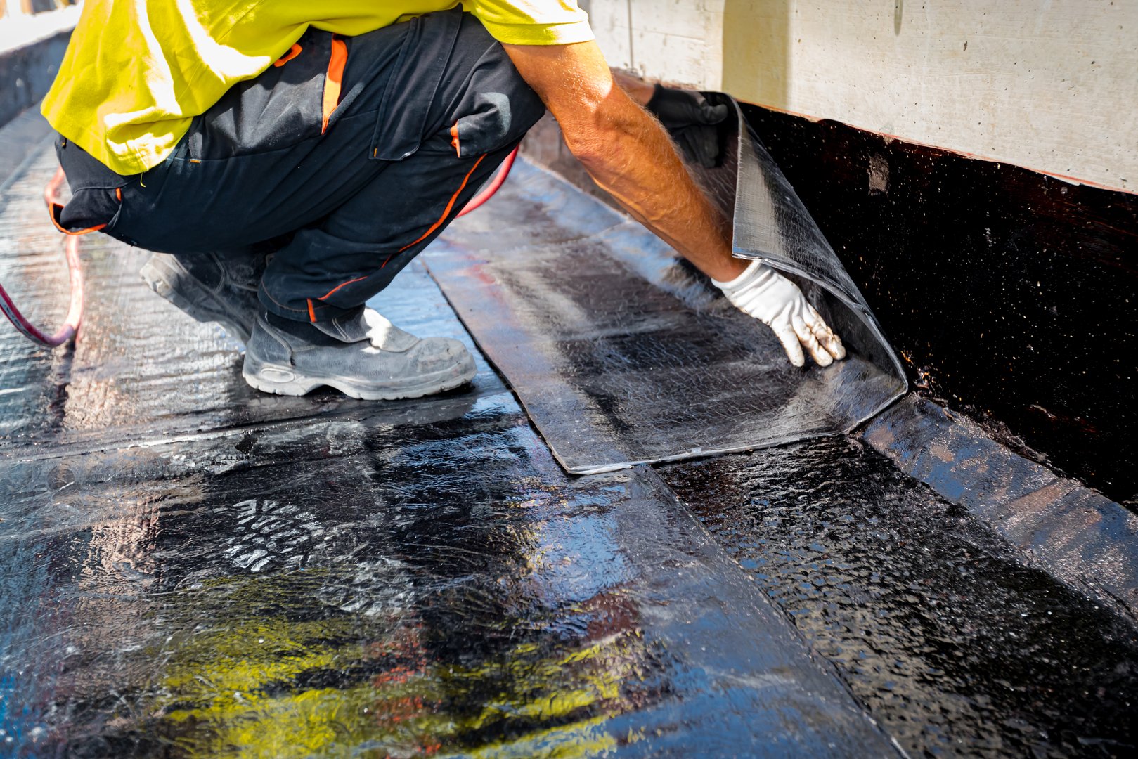 Worker in gloves prepare for melting, manually place and unroll rolled up, sheet of waterproofing installation over concrete. Residential building under construction placing water insulation