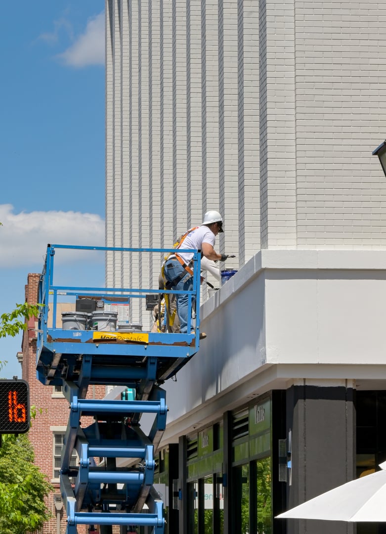 Alexandria, Virginia, USA - 1 May 2024: People standing on a hydraulic scissor lift platform undertaking maintenance work on the outside of a building in the town centre