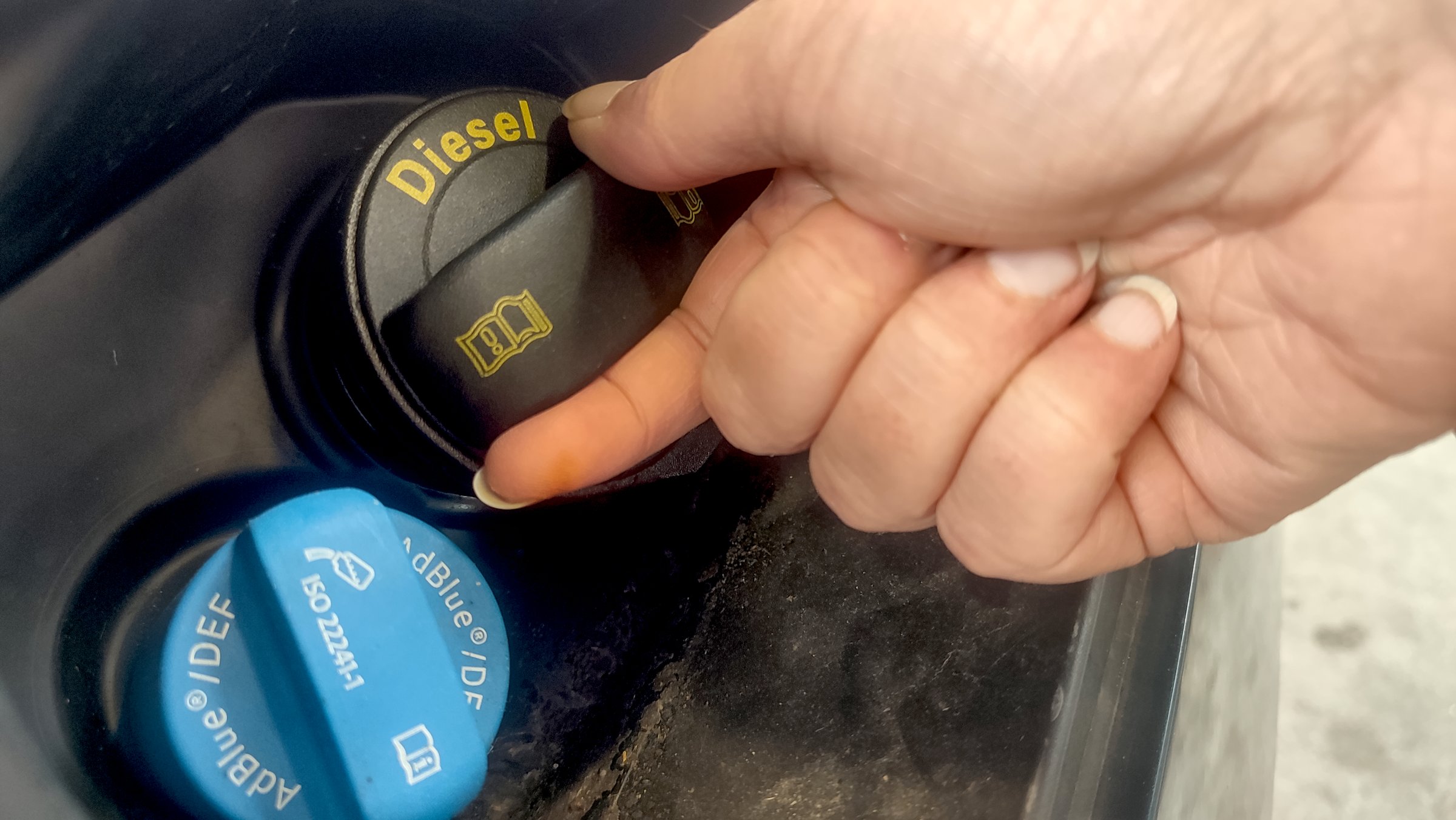 Bellaing, France - 09 20 2025 : Hand opening a diesel fuel cap next to an AdBlue DEF tank at a vehicle refueling station, showing detail of fuel system components.