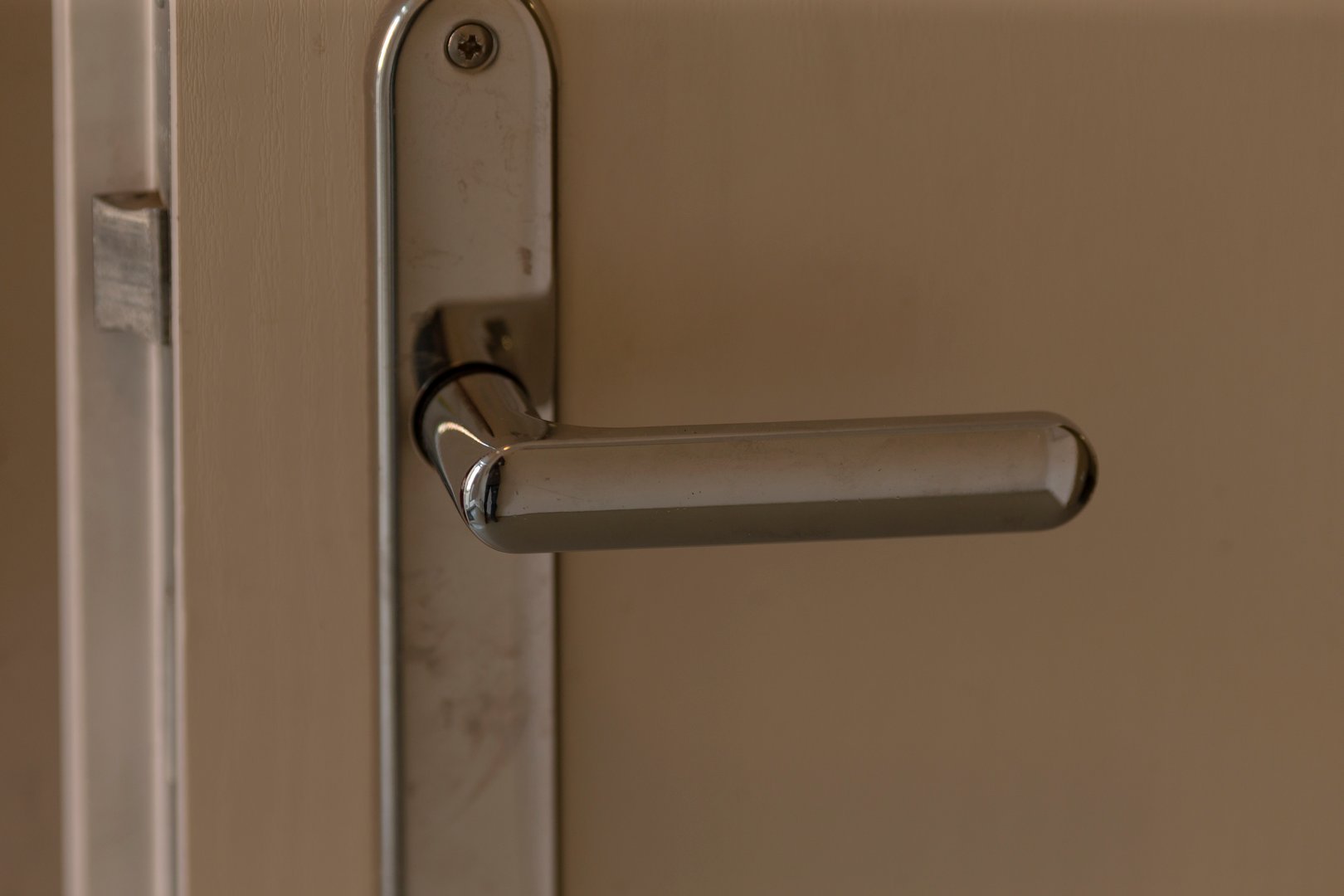 closeup metal door handle on wooden door, soft warm light highlights brushed finish and subtle scratches, modern lever style, focus on lock mechanism and hinge, ambient residential interior mood