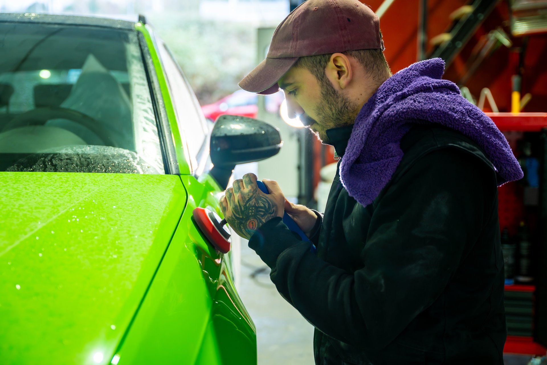 Young adult man working on a bright green car, precisely polishing the bodywork with an orbital buffer for a perfect finish in a professional auto detailing shop