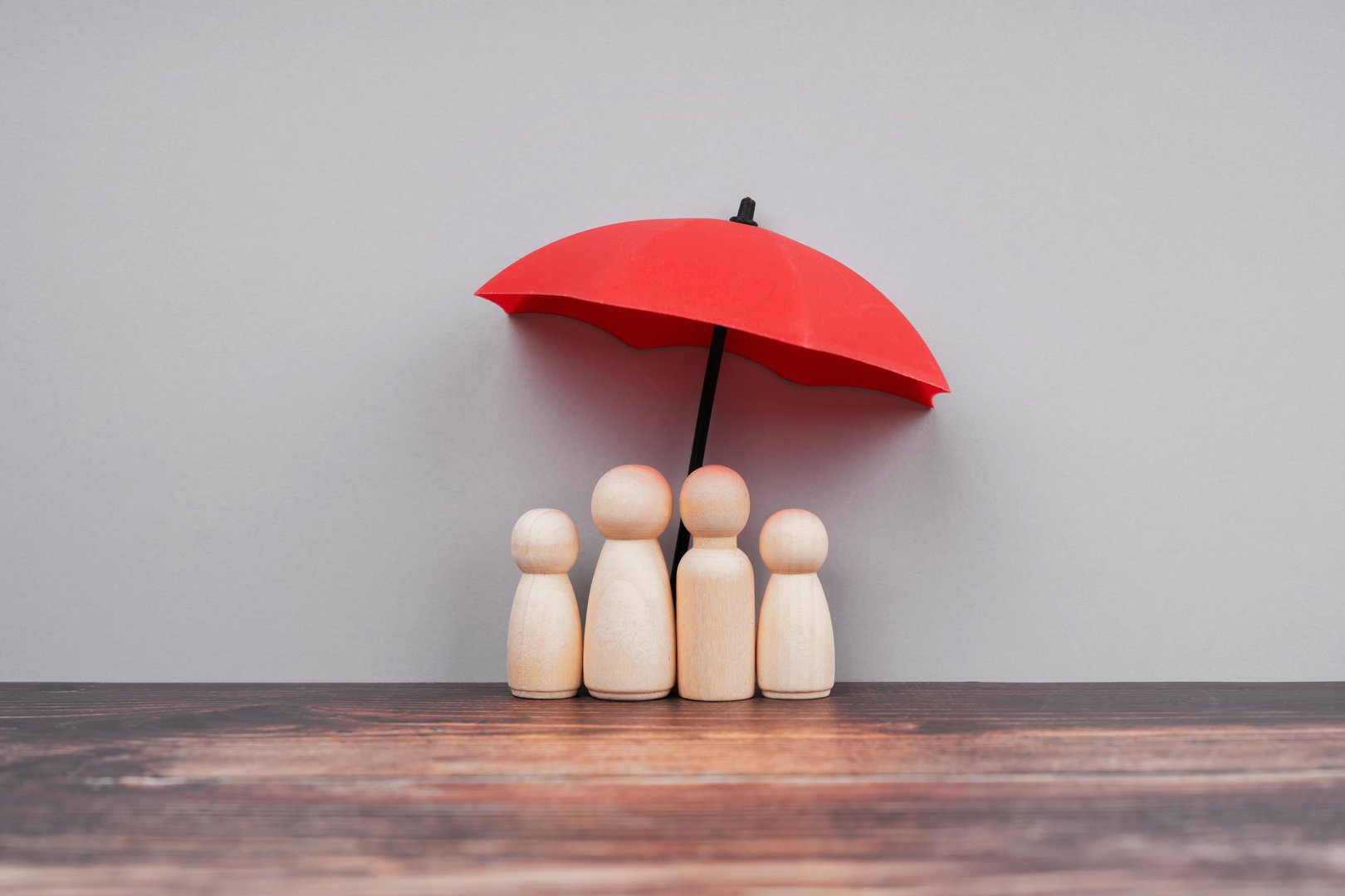 Wooden people represent parent and children under a red umbrella.