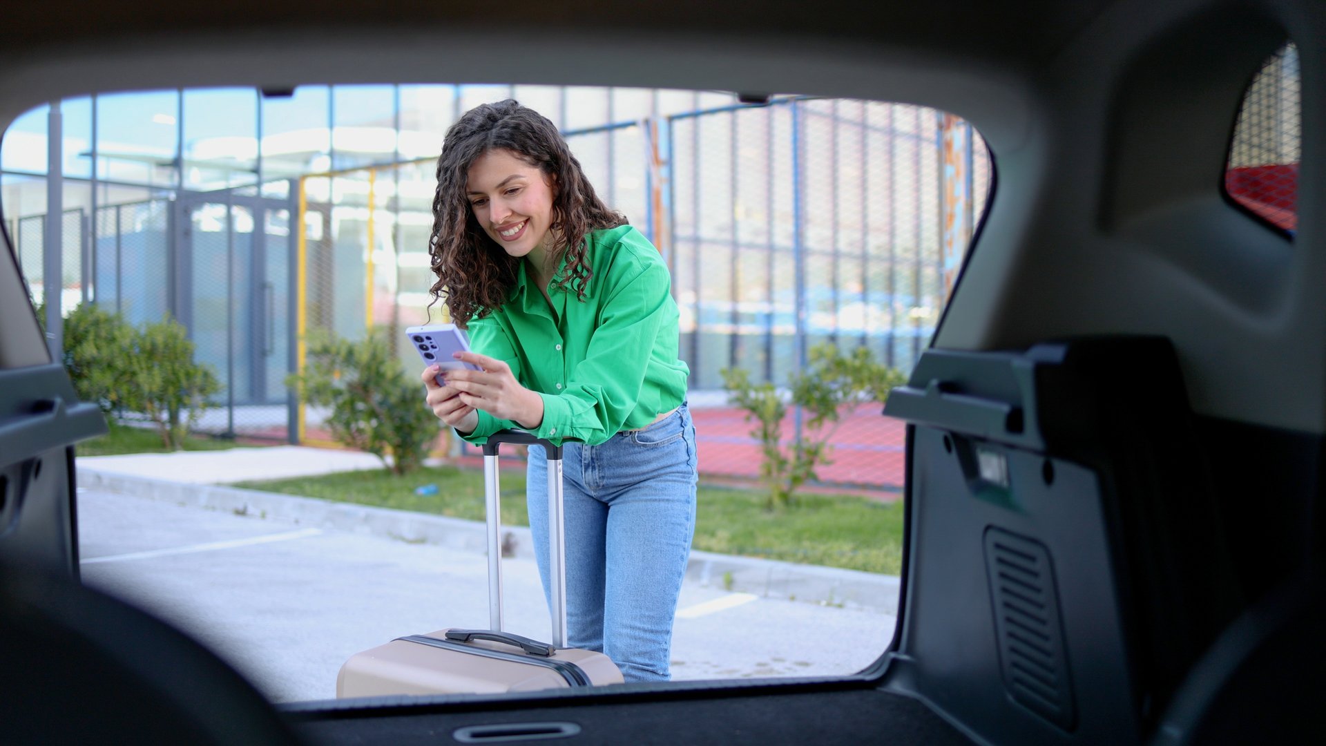 Tourist is using her smartphone while loading luggage into car trunk