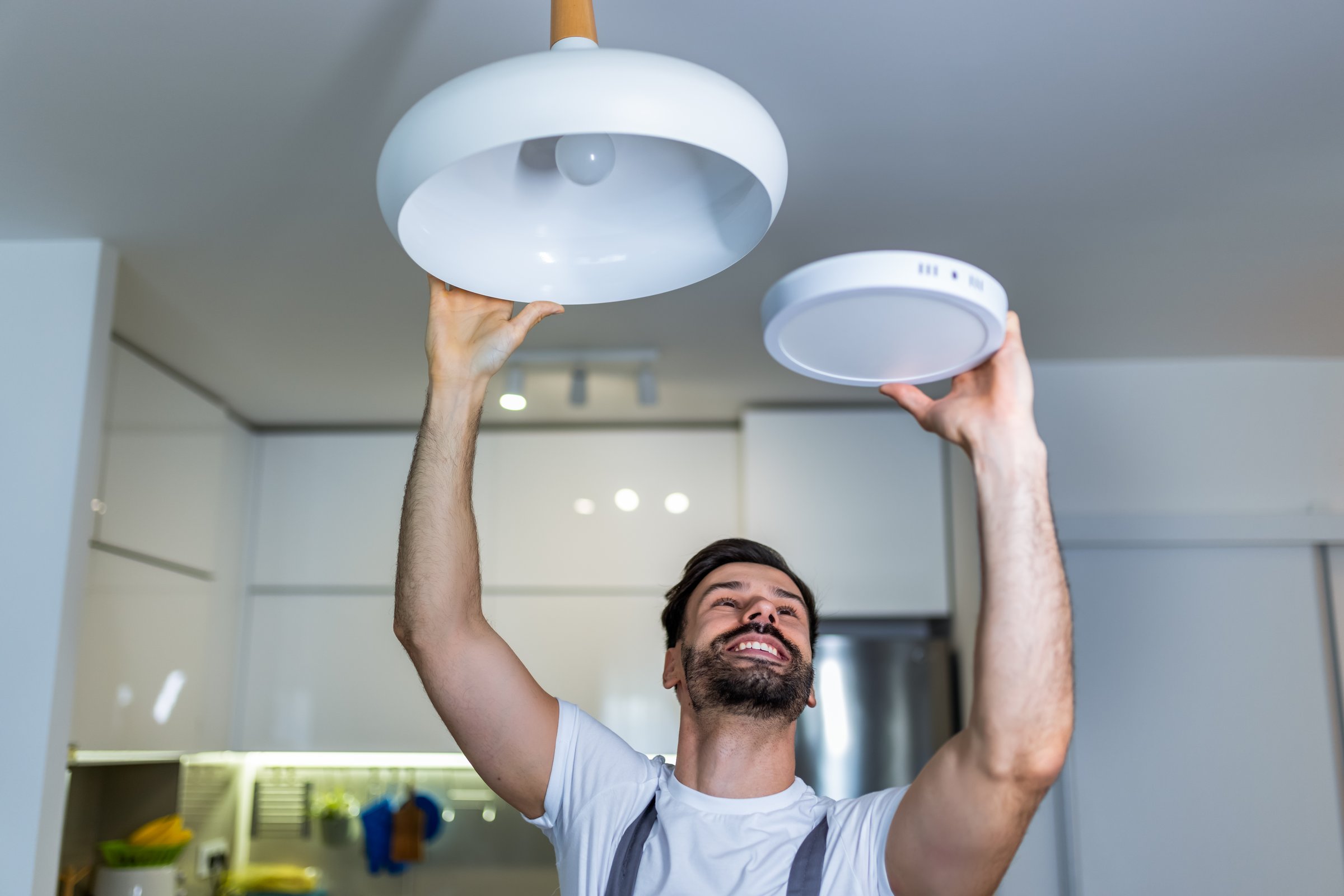 A young handyman is replacing a chandelier with a modern LED panel in an apartment.