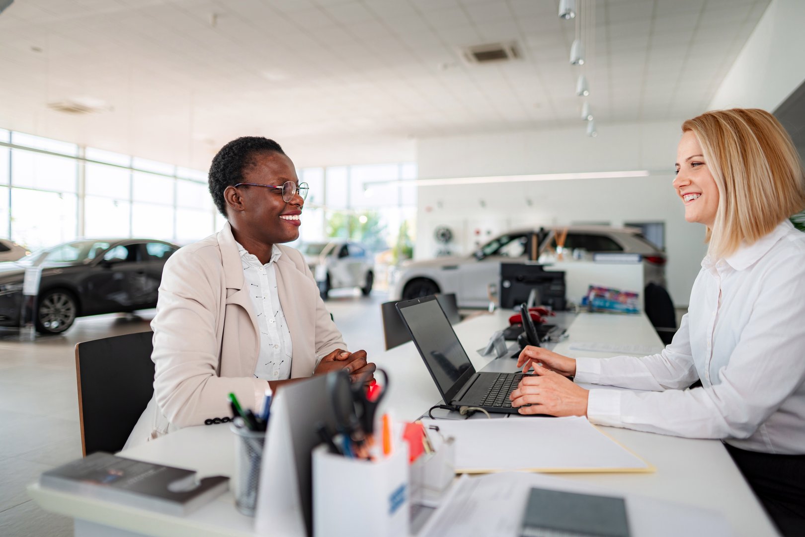 Two women smiling and having a business discussion at a car dealership