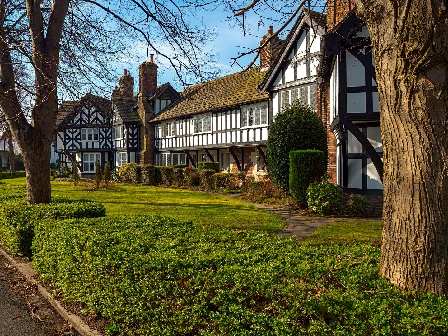 A row of old timber framed black buildings with a green lawn in front of them. The scene has a peaceful and serene atmosphere