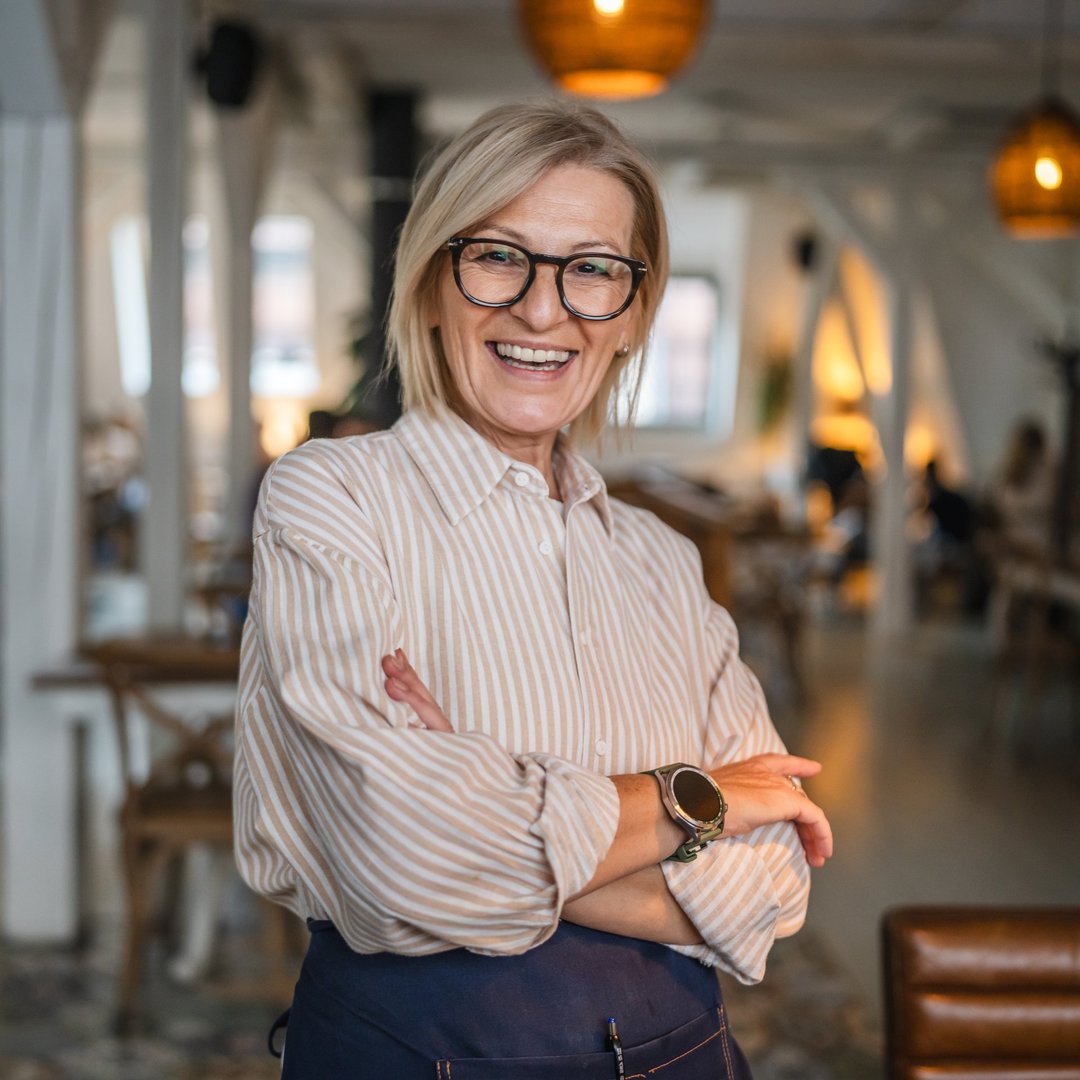 Portrait of a happy mature woman stand at restaurant arm crossed, beautiful woman owner stand and smile at restaurant