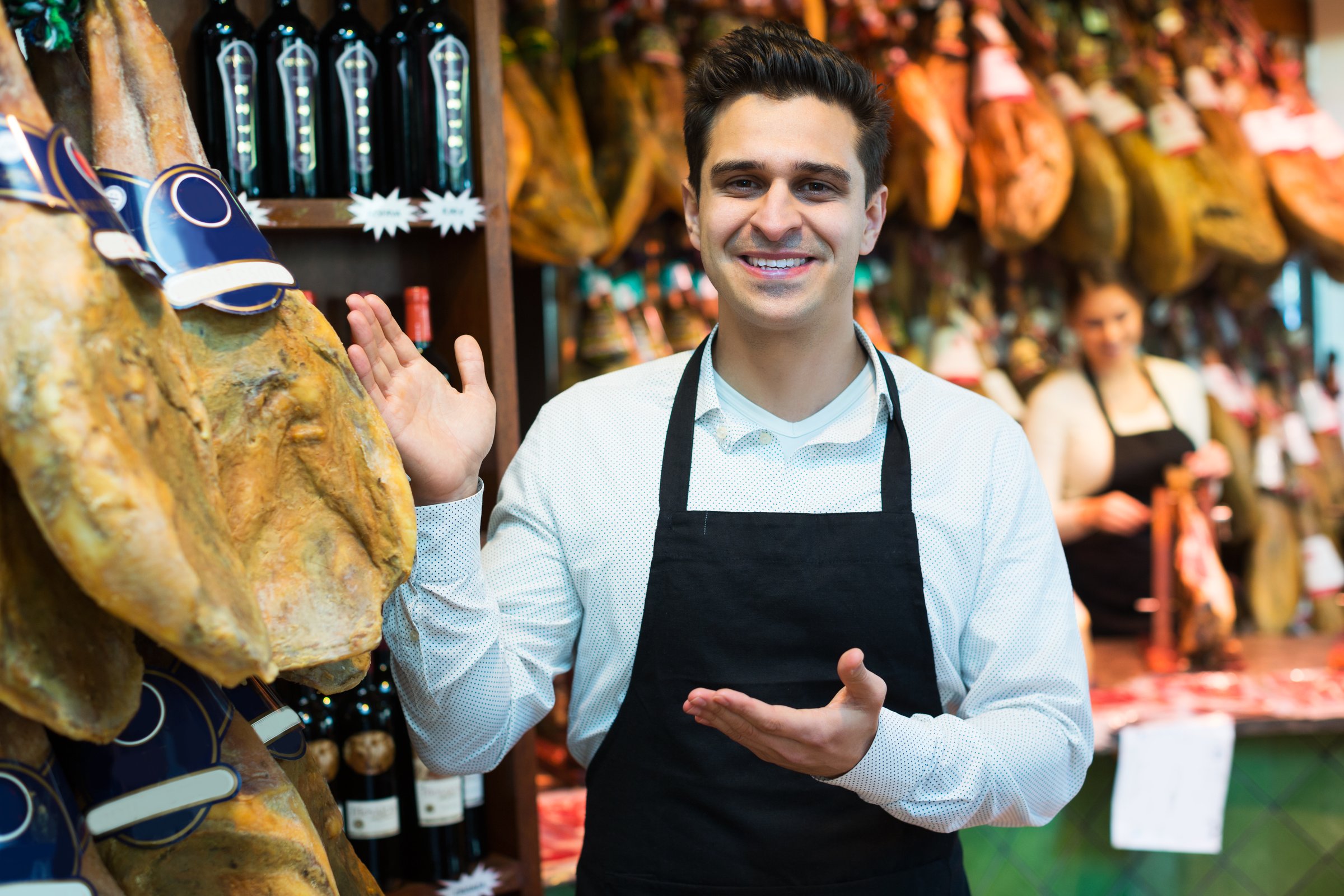 Adult seller man in delicatessen section with iberico and serrano jamon