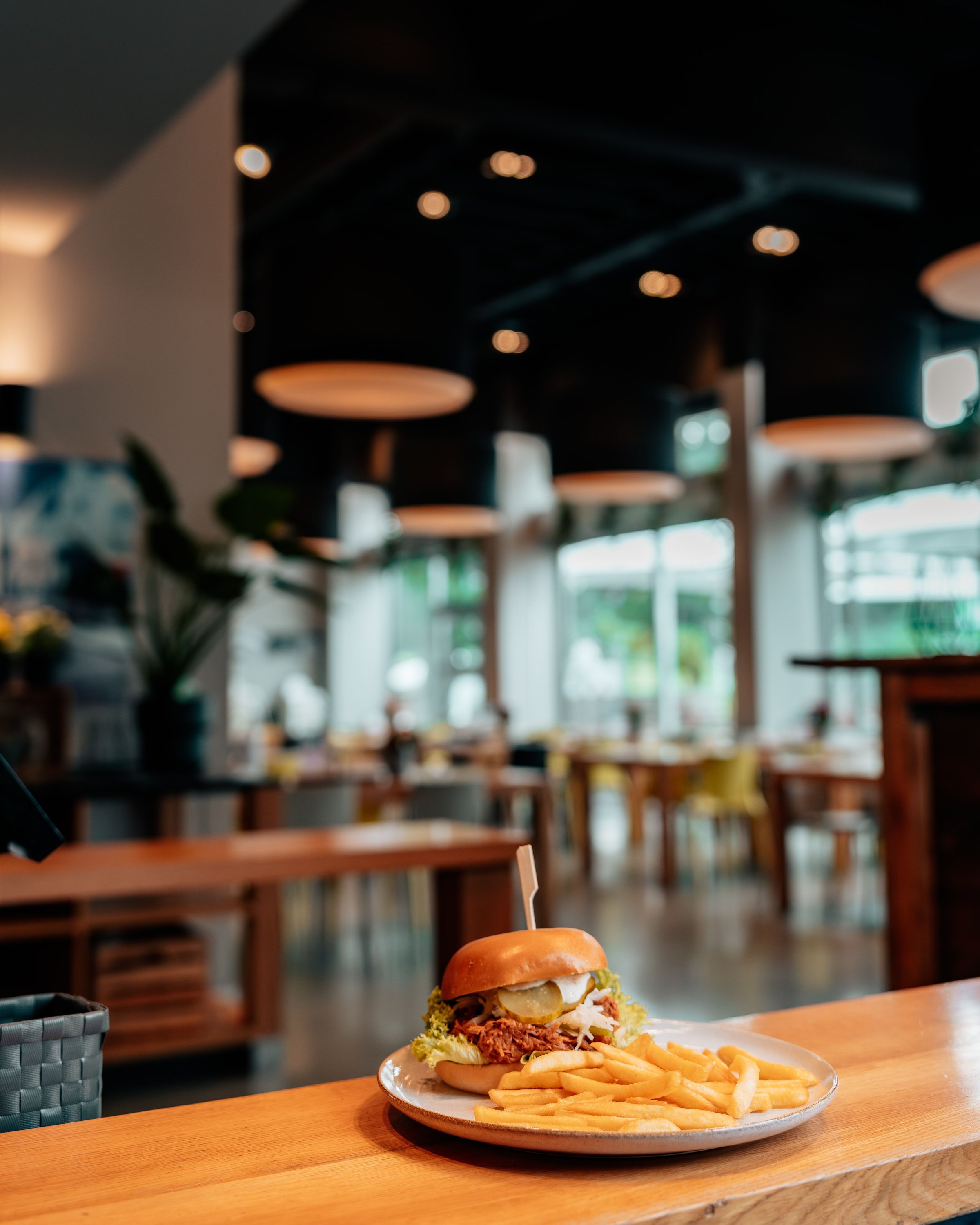 A delicious burger with fries on a wooden table in a modern restaurant setting, featuring soft lighting and contemporary decor.