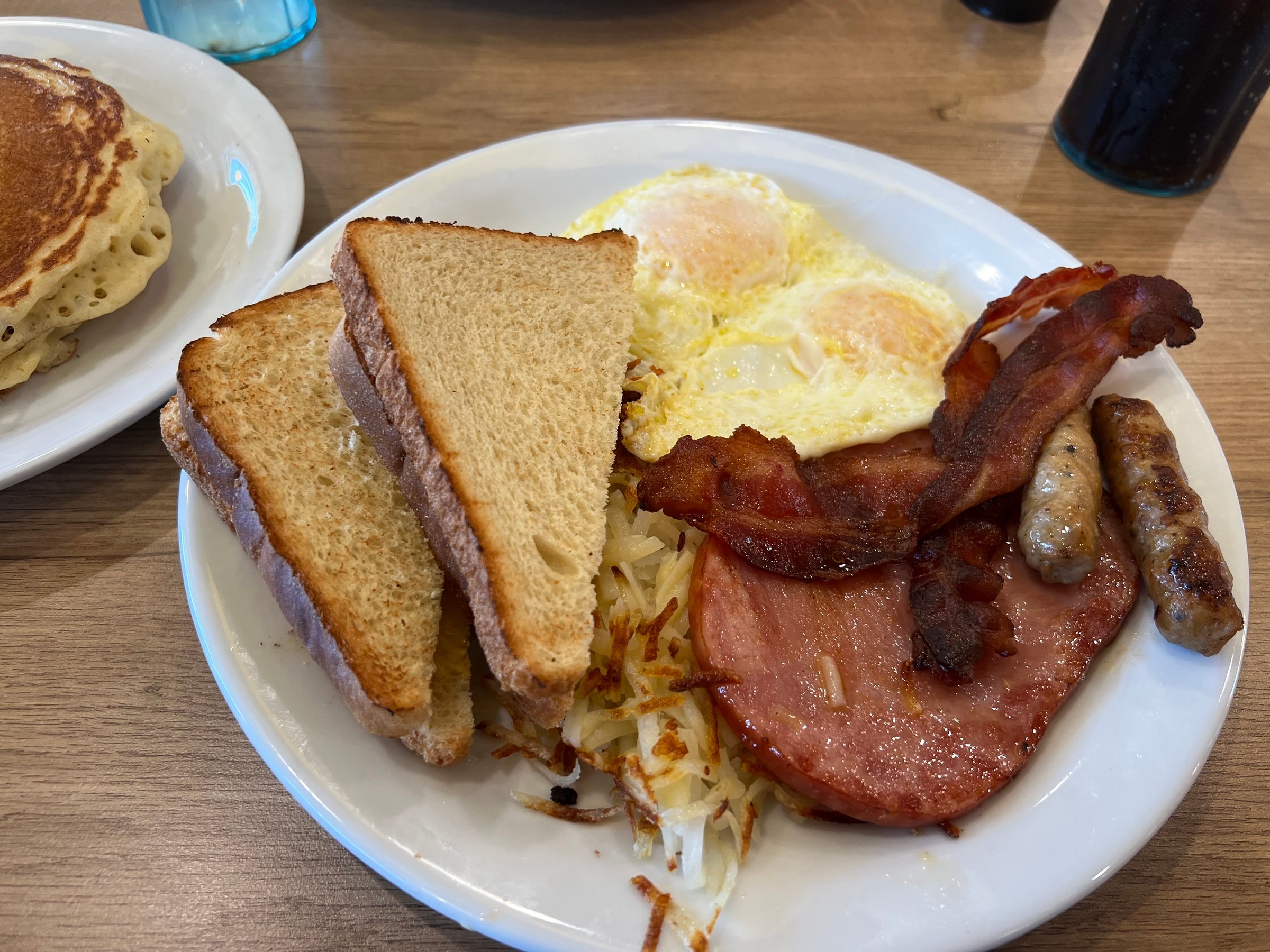 A hearty breakfast plate with eggs bacon sausage ham hashbrowns and toast served with a side of pancakes